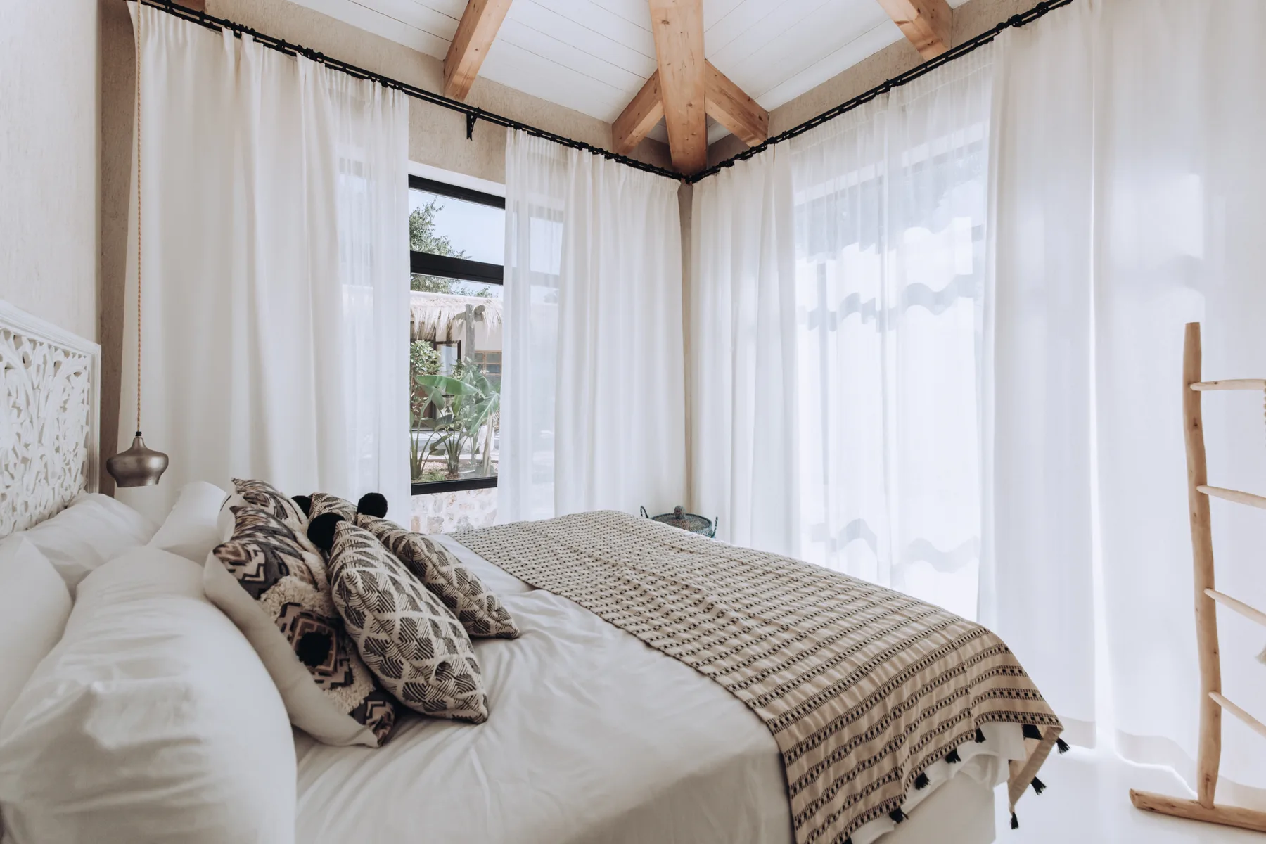 A bright bedroom with a bed and large curtained windows.