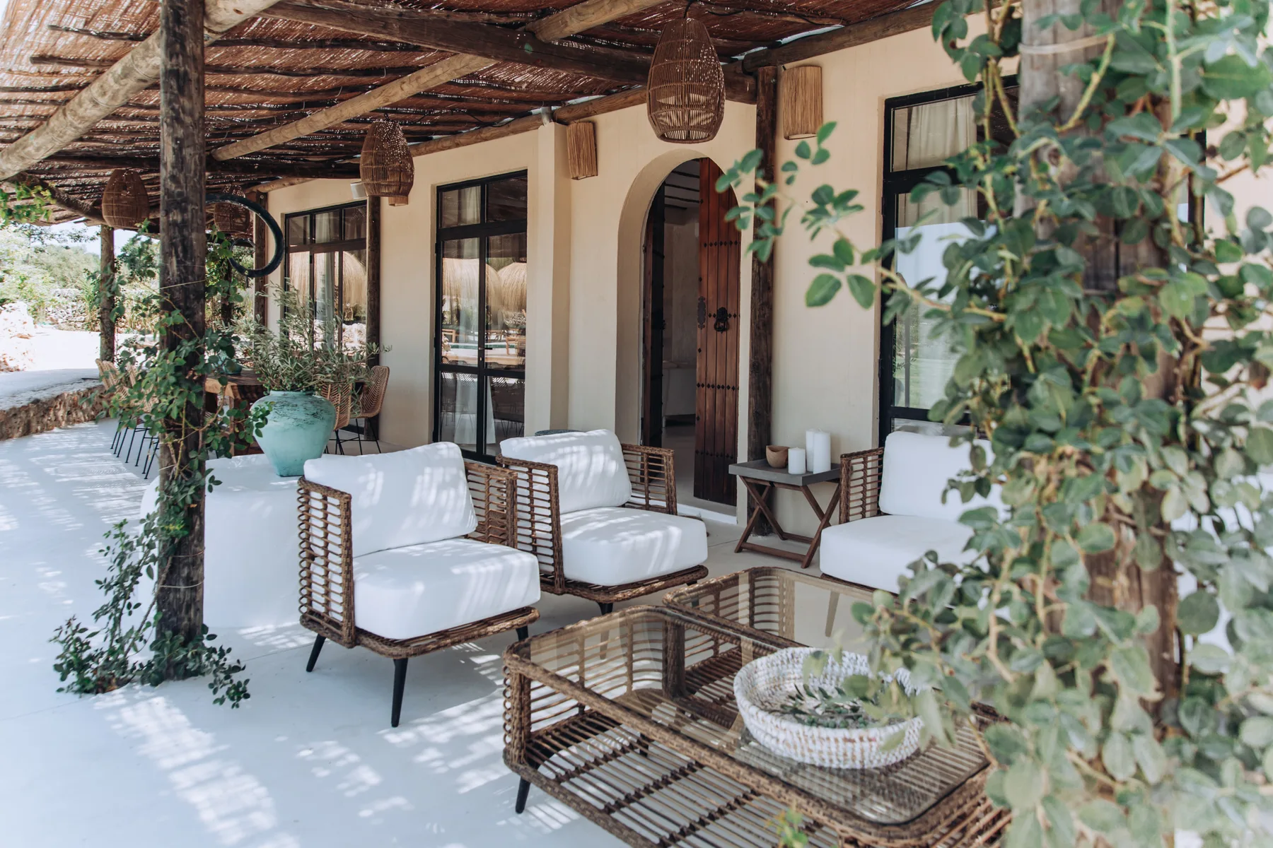 A covered patio with cushioned seating and a low table beside the house.