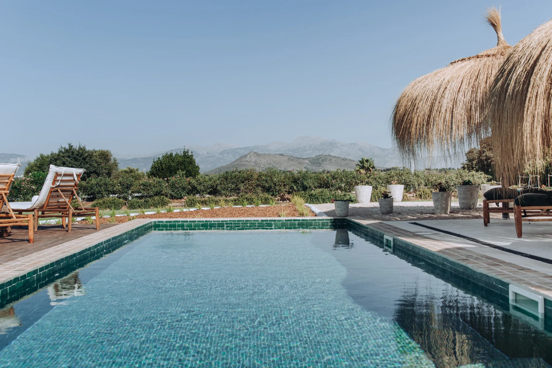 A swimming pool beside a patio, with lounge seating and a thatched shade canopy.