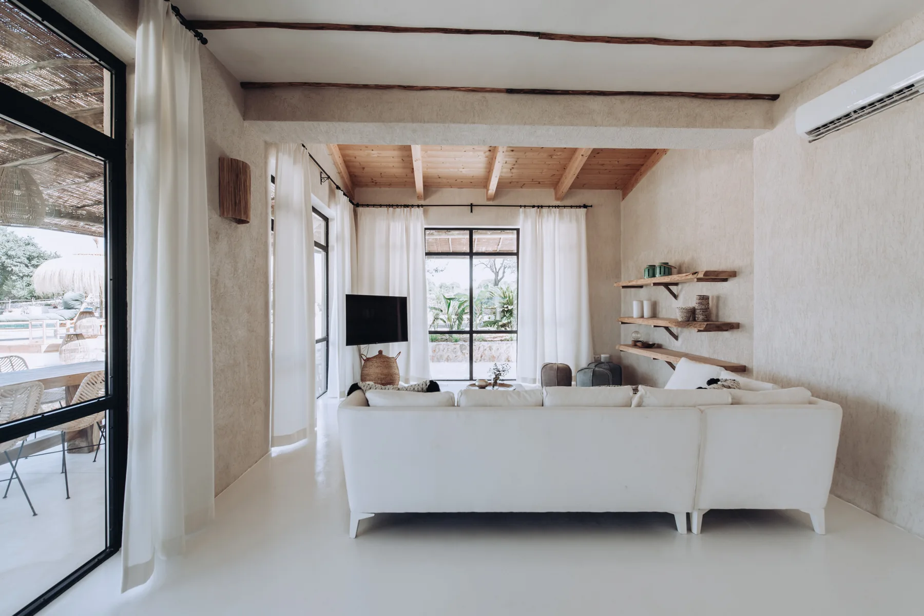 A bright living room with seating arranged around a television and large windows.