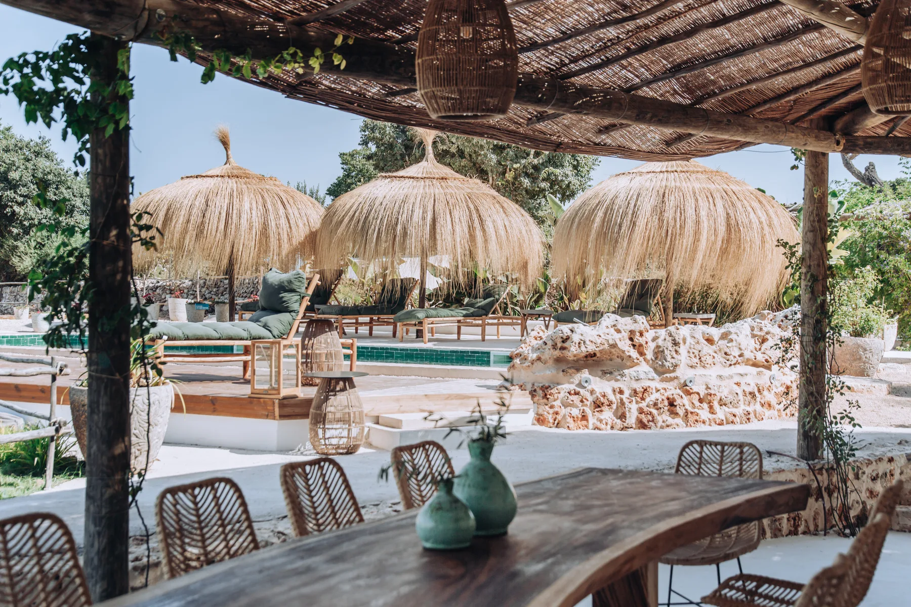 An outdoor poolside seating area sits beneath shaded canopies and a woven pergola.