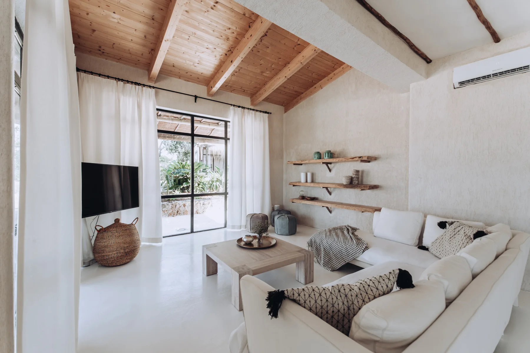 A bright living room with white seating, a coffee table, and a large window.