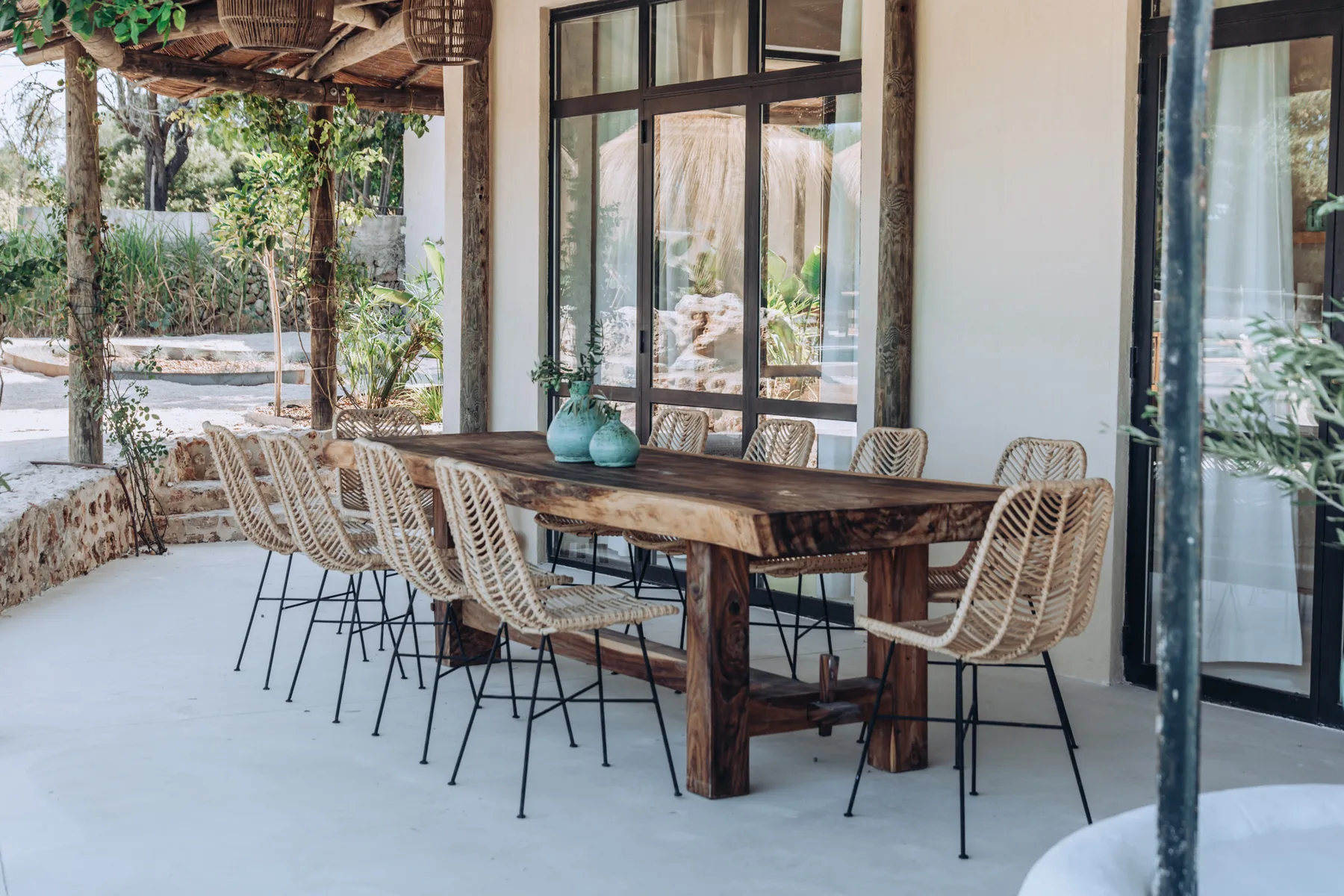 A covered outdoor dining area with a long wooden table and woven seating.