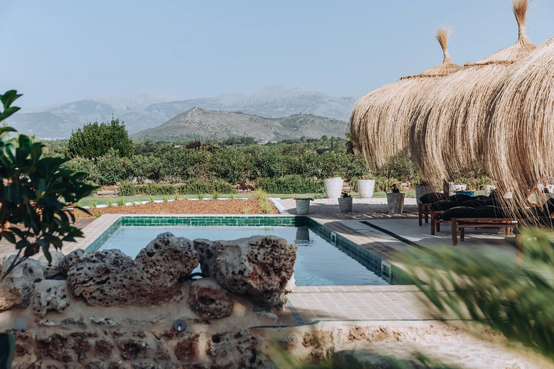 An outdoor swimming pool sits beside shaded seating, with hills in the distance.