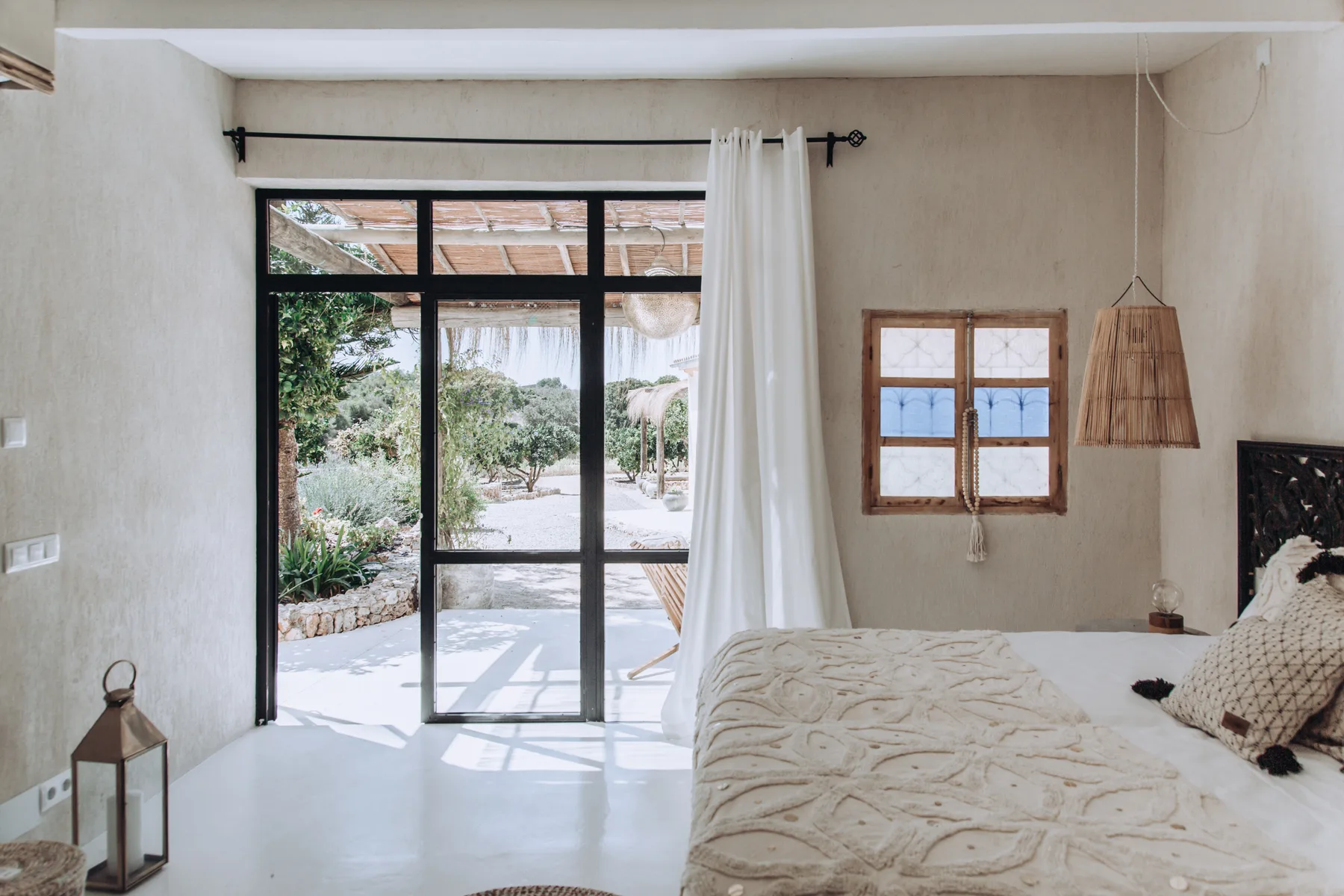 A bedroom with a bed beside a large glass door opening onto a garden.
