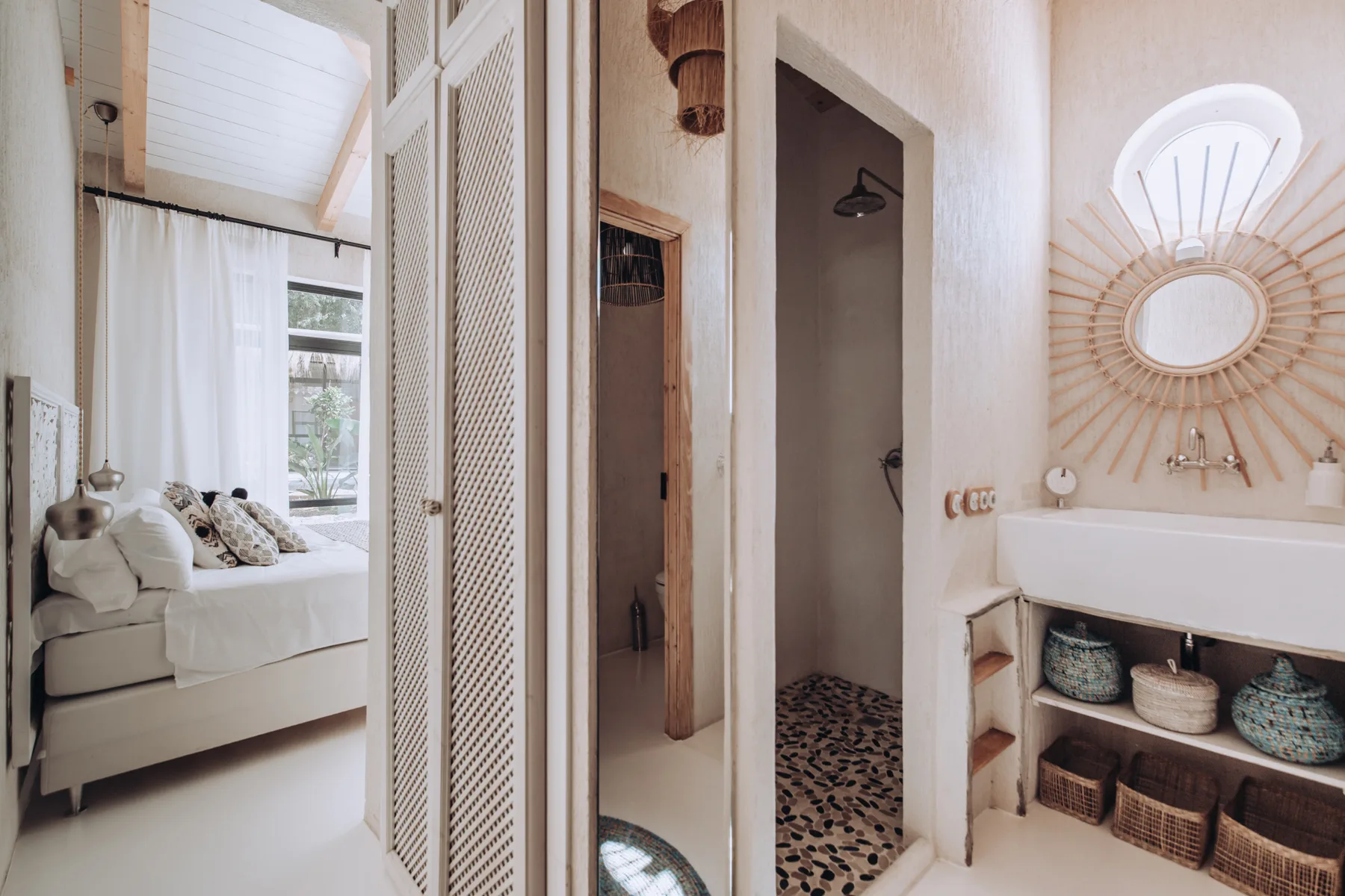 A bright interior shows a bedroom beside a bathroom with a sink and round mirror.