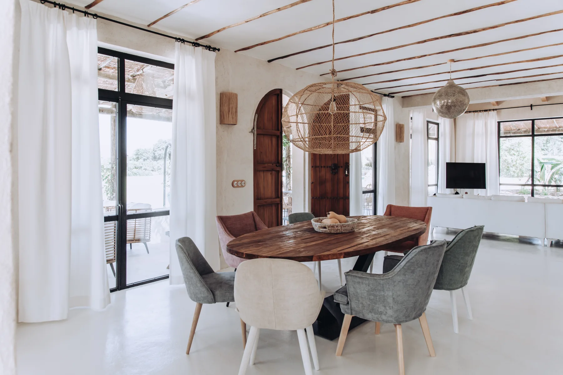 A dining area with a wooden table and chairs beside large windows.