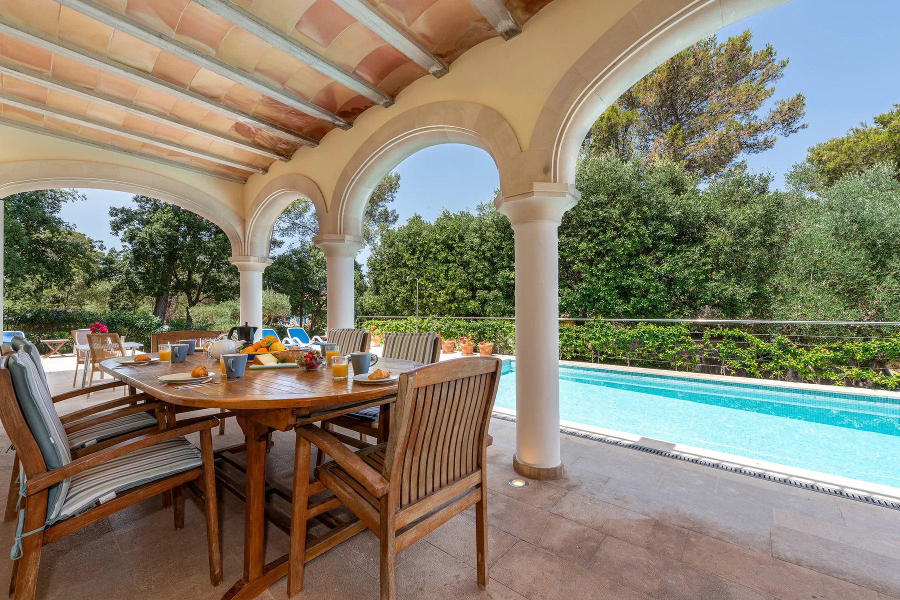 A covered outdoor dining area overlooks a swimming pool and garden.