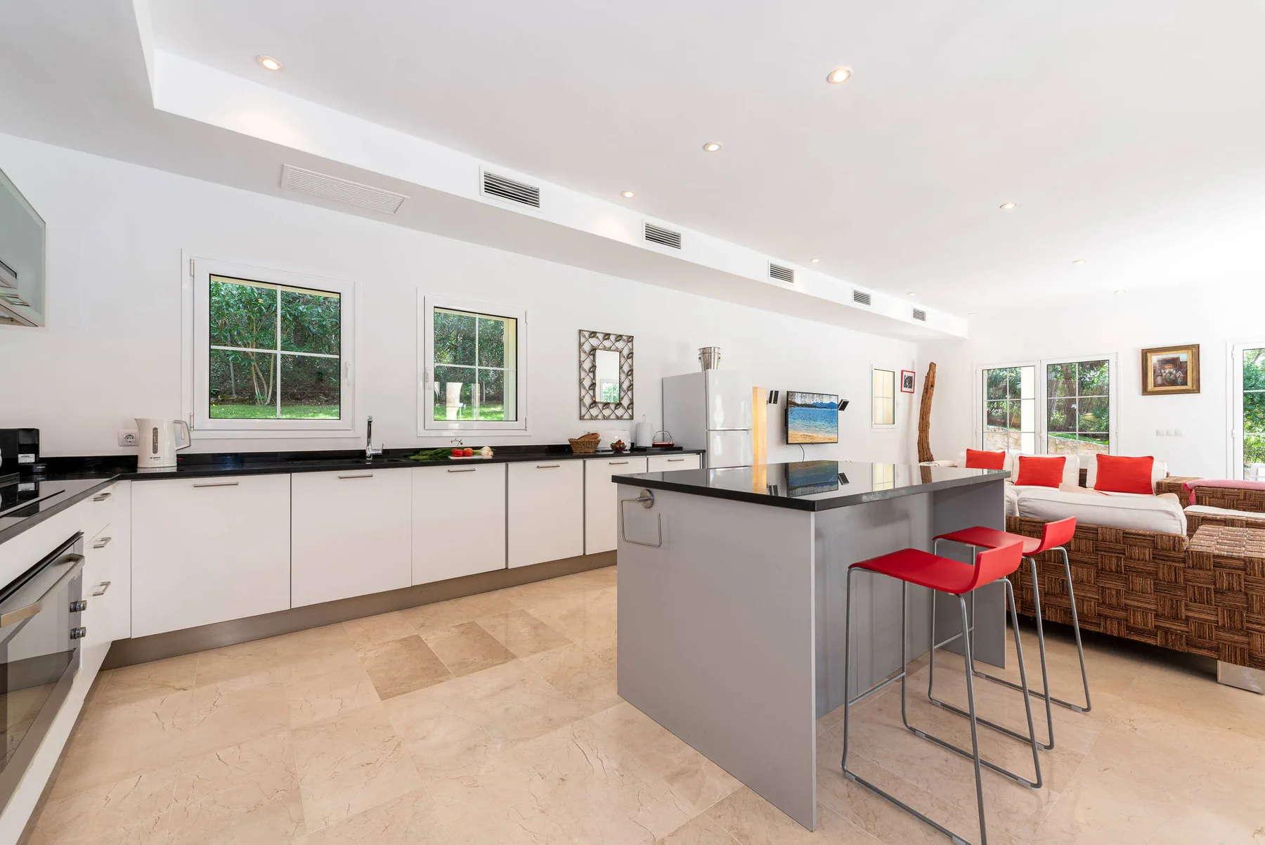 A bright open-plan kitchen and dining area with a central island and red stools.