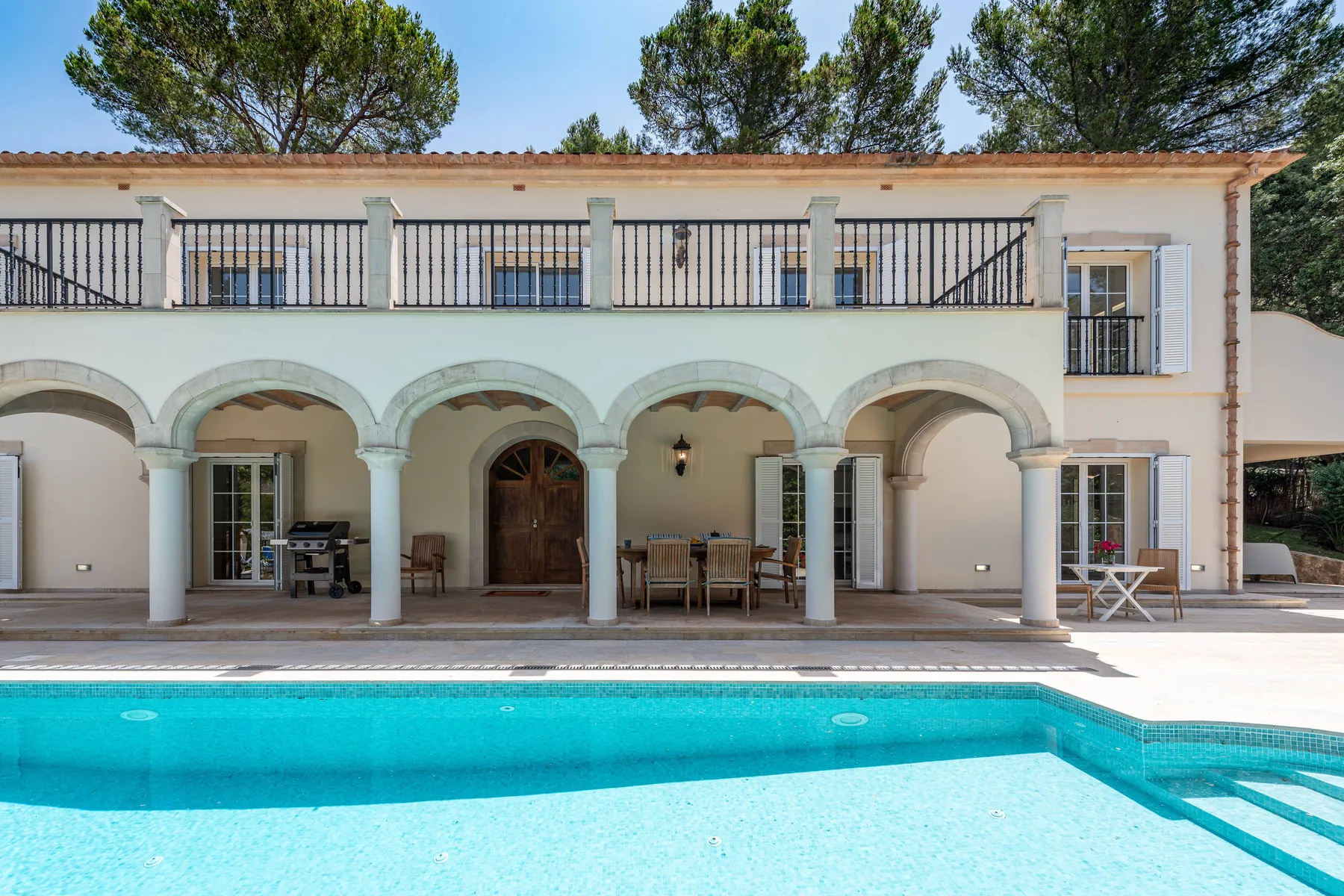 A two-story house with an arched patio overlooks a swimming pool.