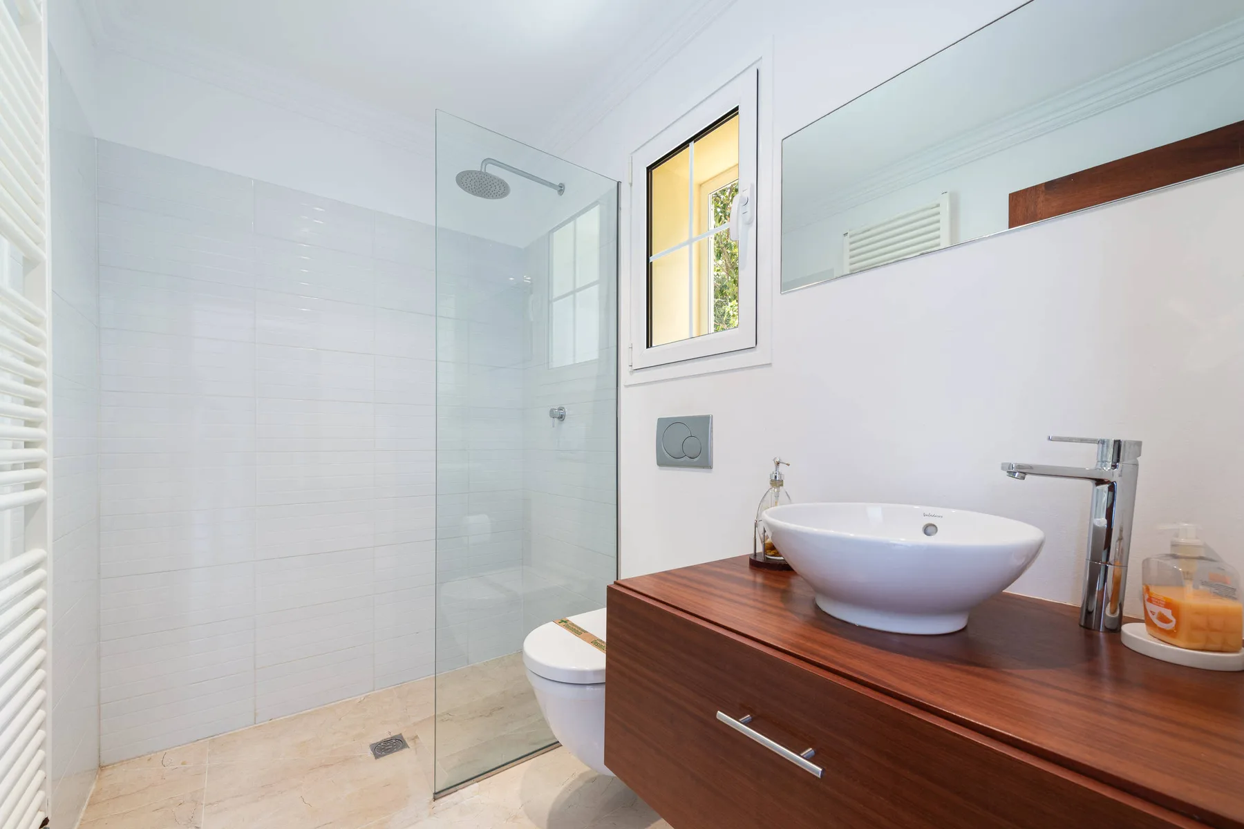 A bright bathroom with a glass shower, basin, and wooden vanity.