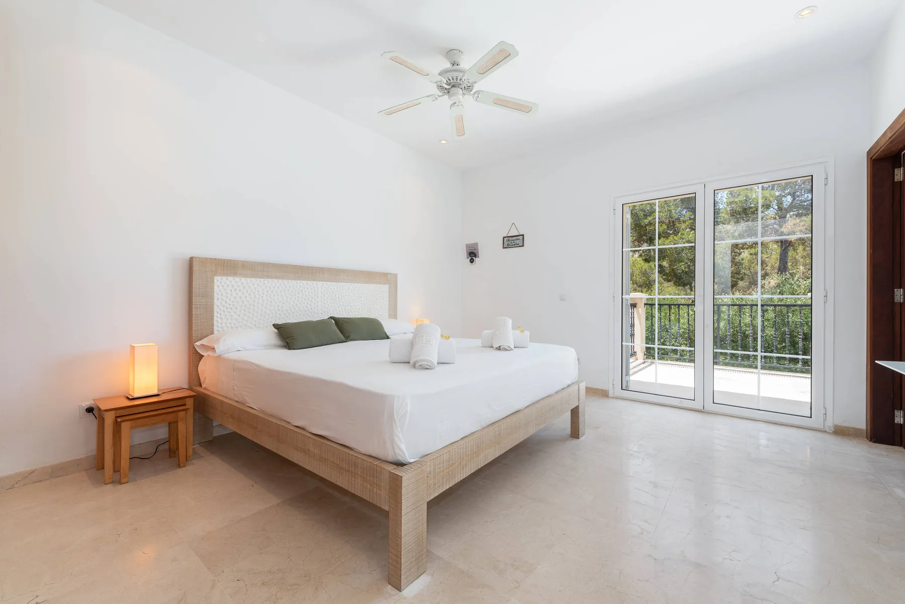 A bright bedroom with a neatly made bed and glass doors opening onto a balcony.