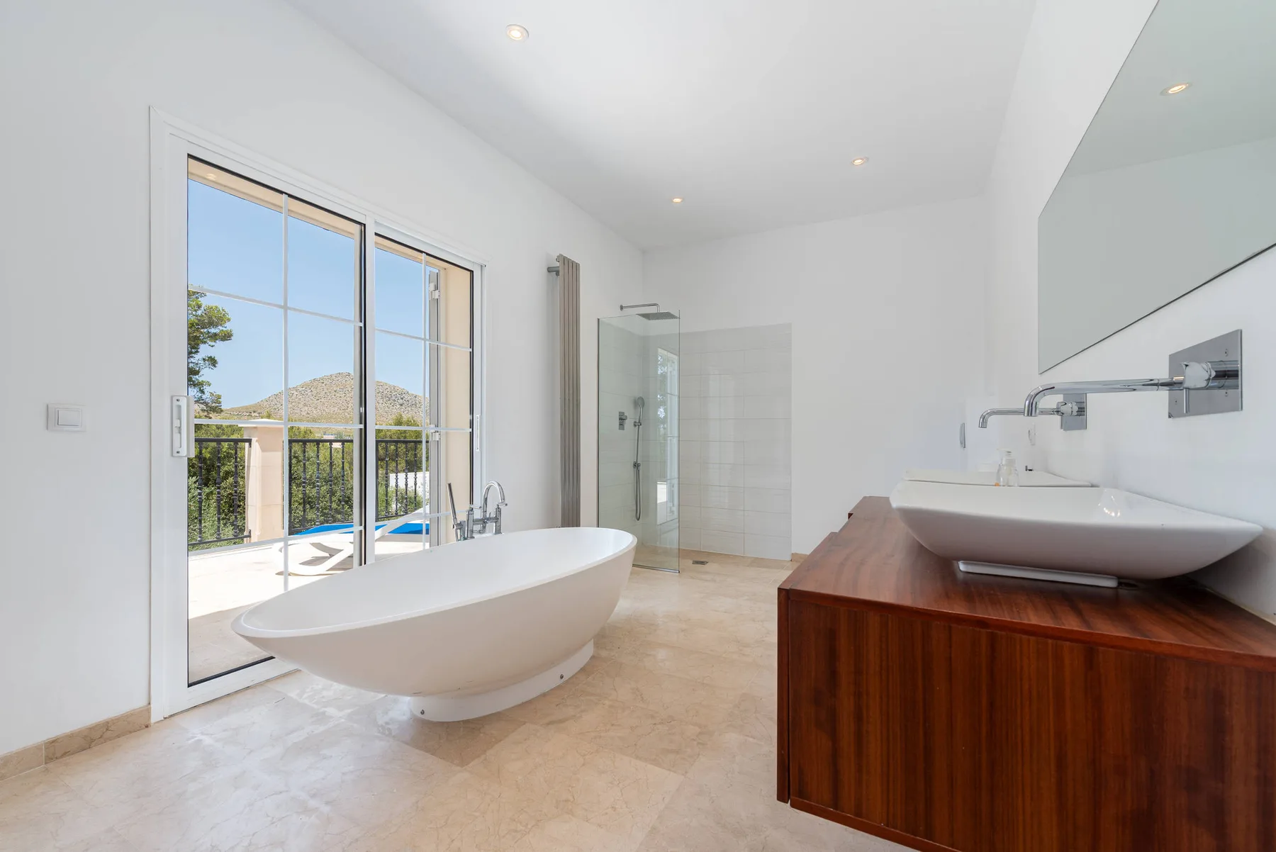 A bright bathroom with a freestanding bathtub and a vanity beside large glass doors.