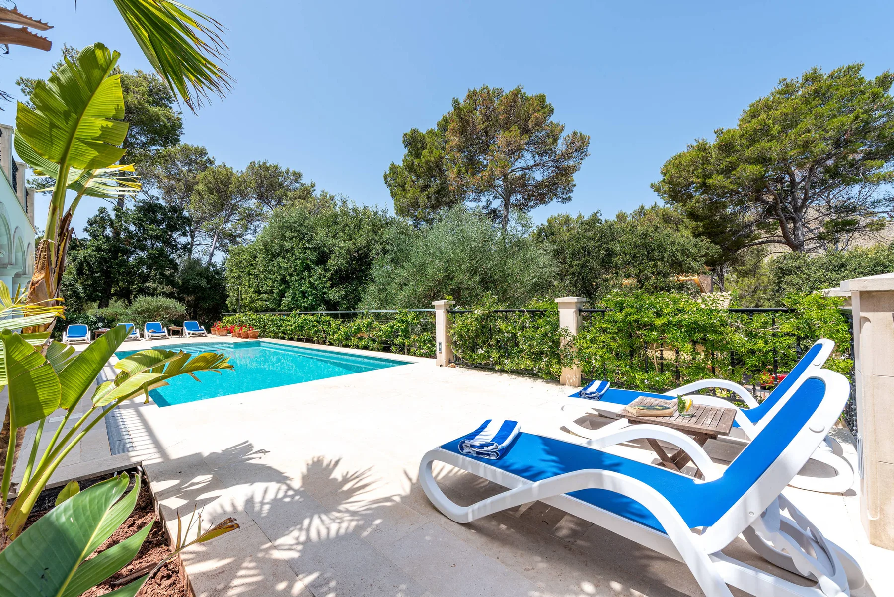 An outdoor swimming pool beside a paved patio with blue lounge seating.