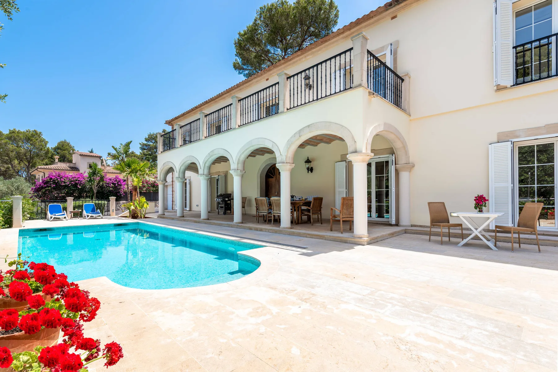 A swimming pool and patio sit beside a house with an arched veranda.