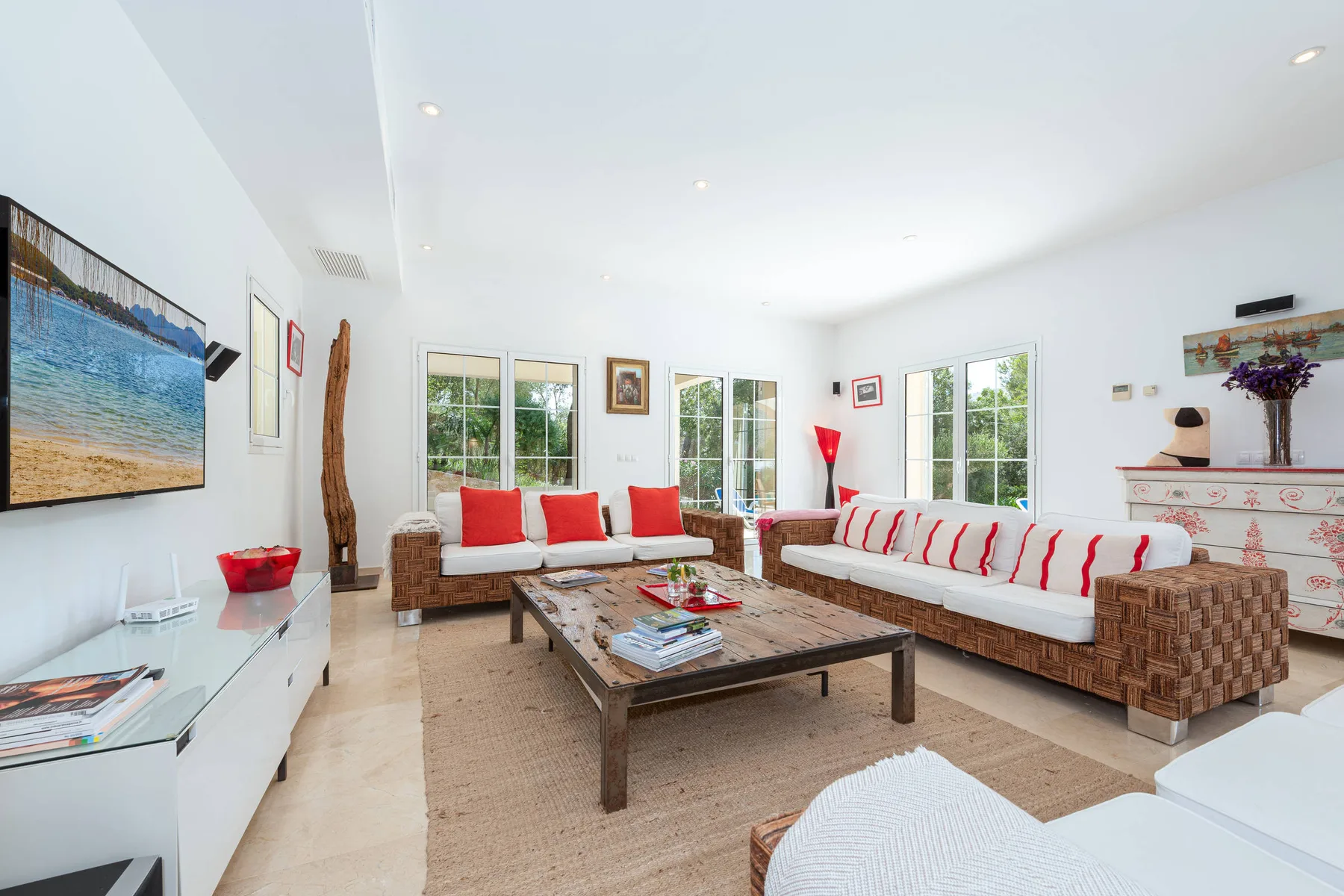 A bright living room has wicker seating with red-and-white cushions around a wooden coffee table.