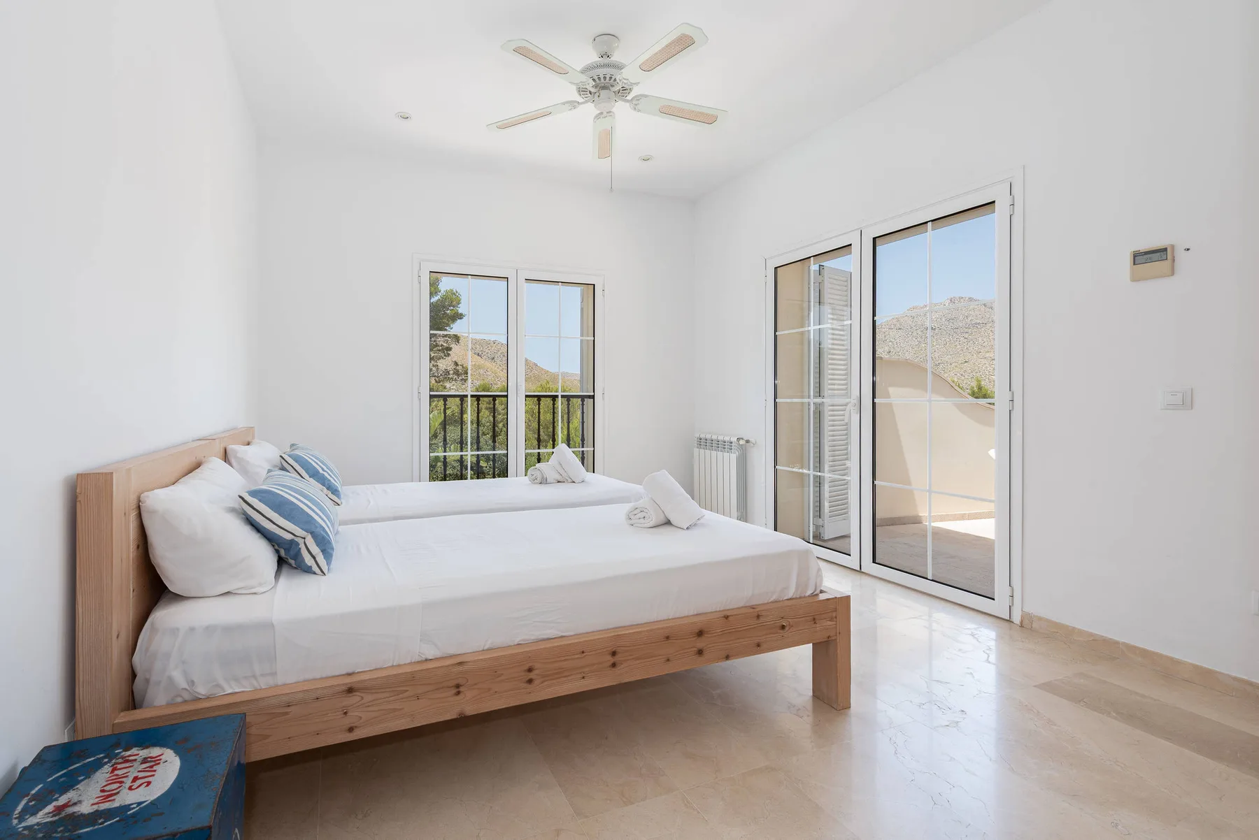 A bright bedroom with a wooden bed and large windows opening onto a balcony.