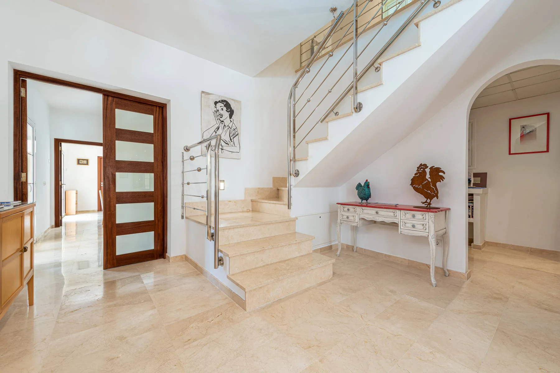 A bright interior foyer with a staircase, a console table, and an open doorway.