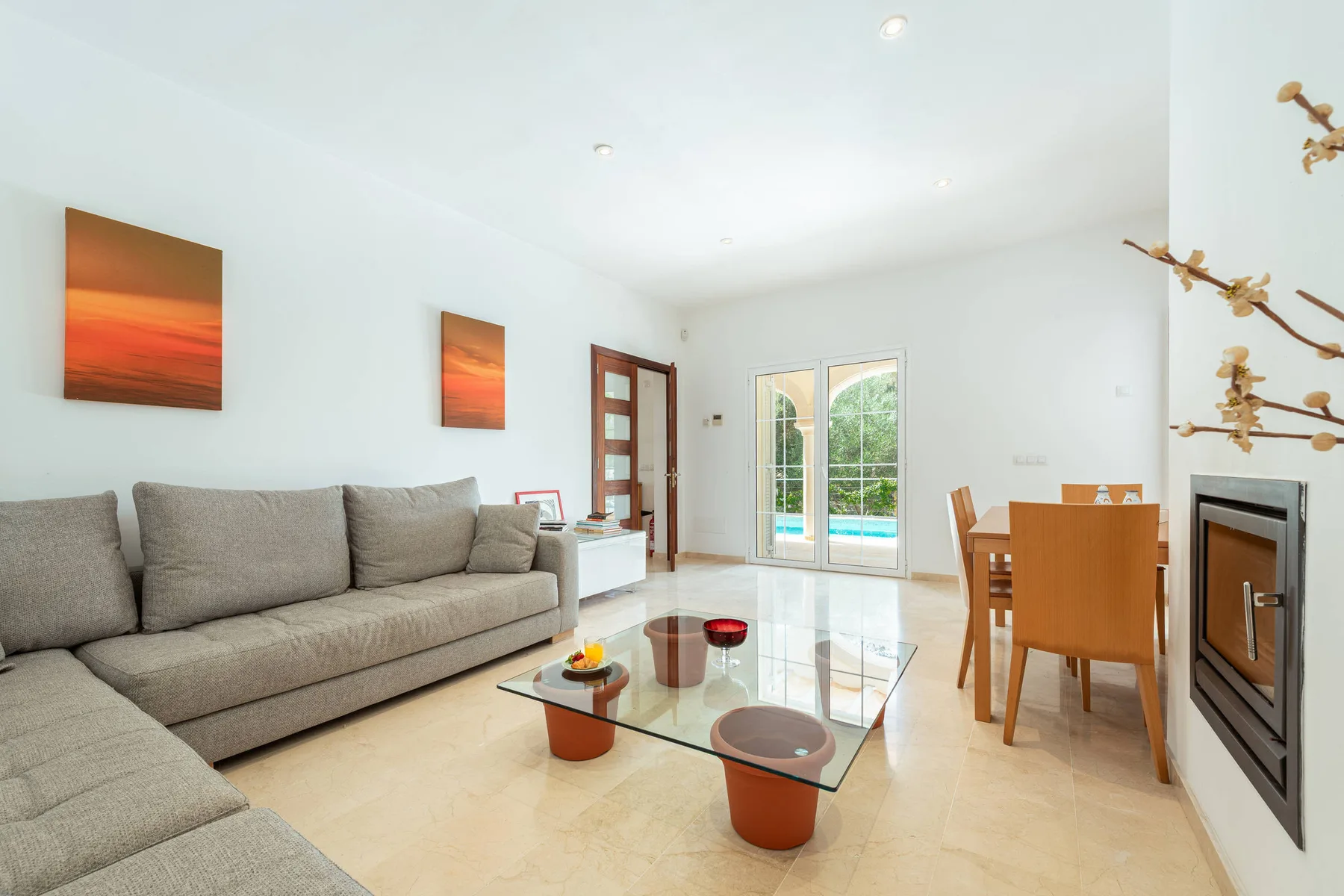 A bright living and dining room with seating, a glass coffee table, and patio doors.