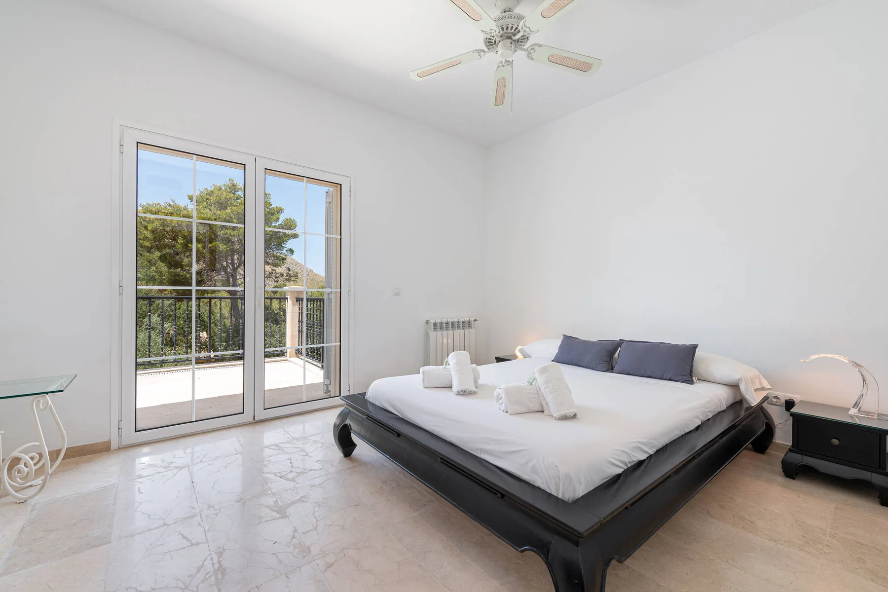 A bright bedroom with a large bed beside glass doors opening onto a balcony.