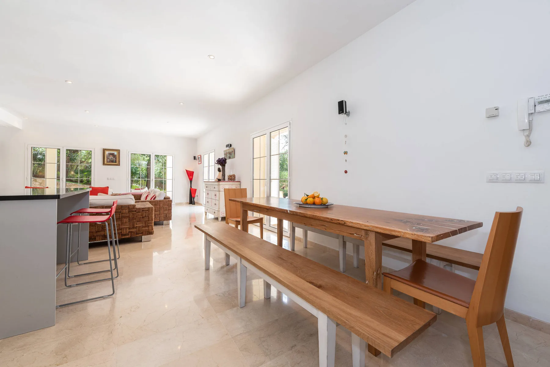 A bright dining area with a long wooden table and benches beside an open kitchen.