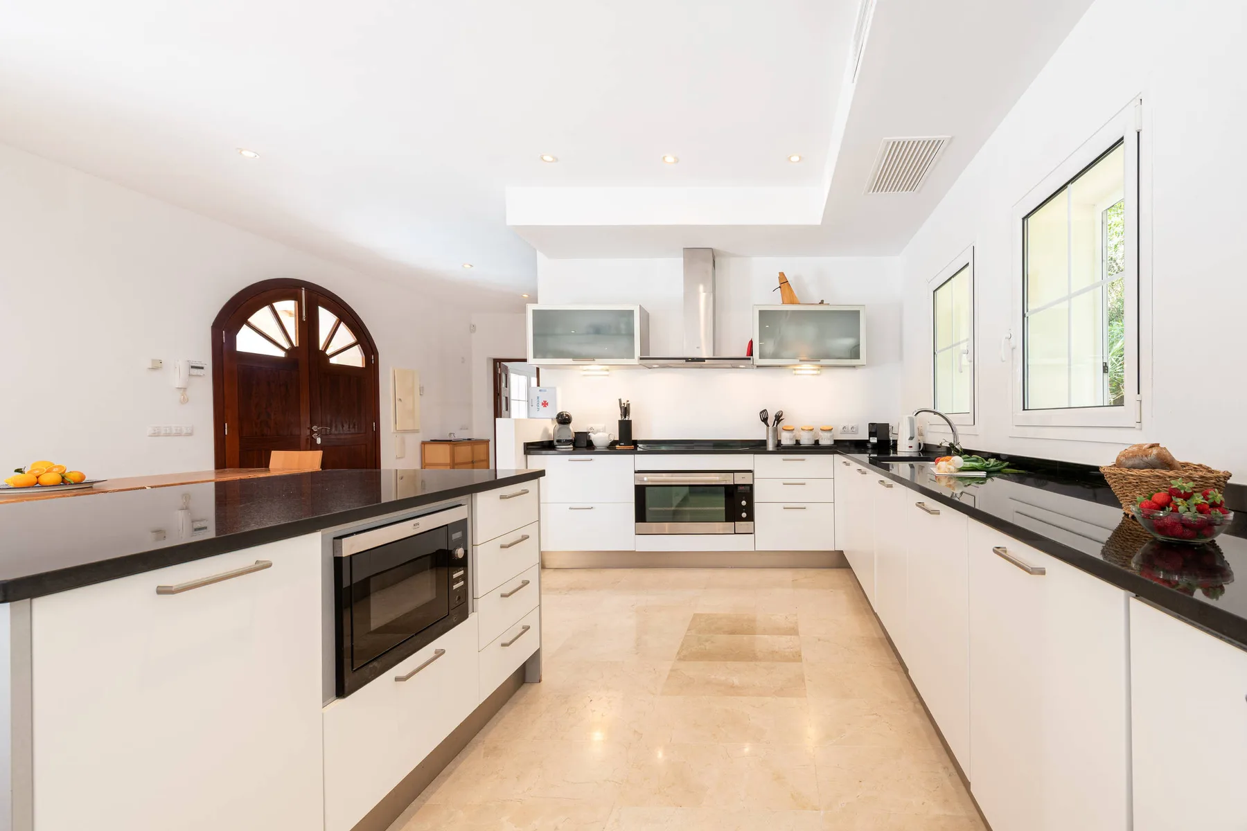 A bright modern kitchen with white cabinetry, dark countertops, and a central island.
