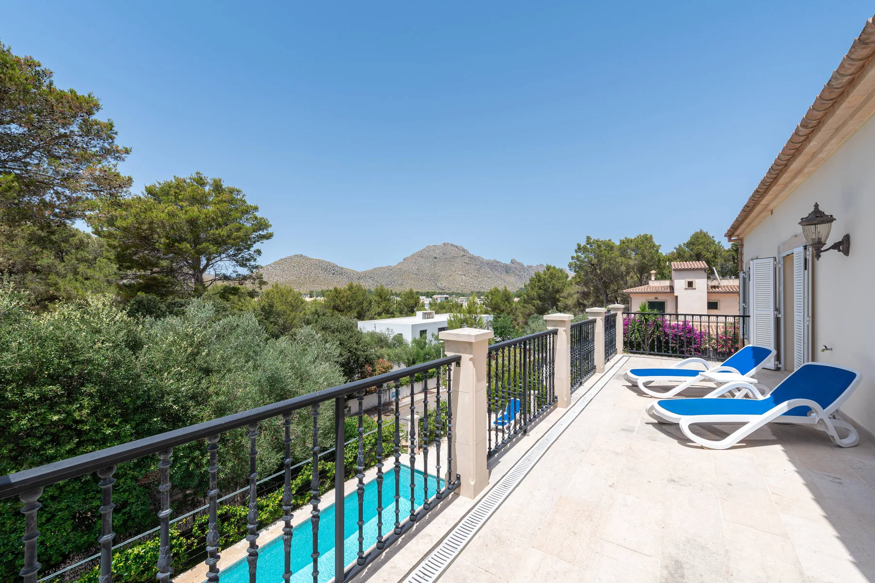 A sunny outdoor terrace overlooks a pool, green trees, and distant hills.