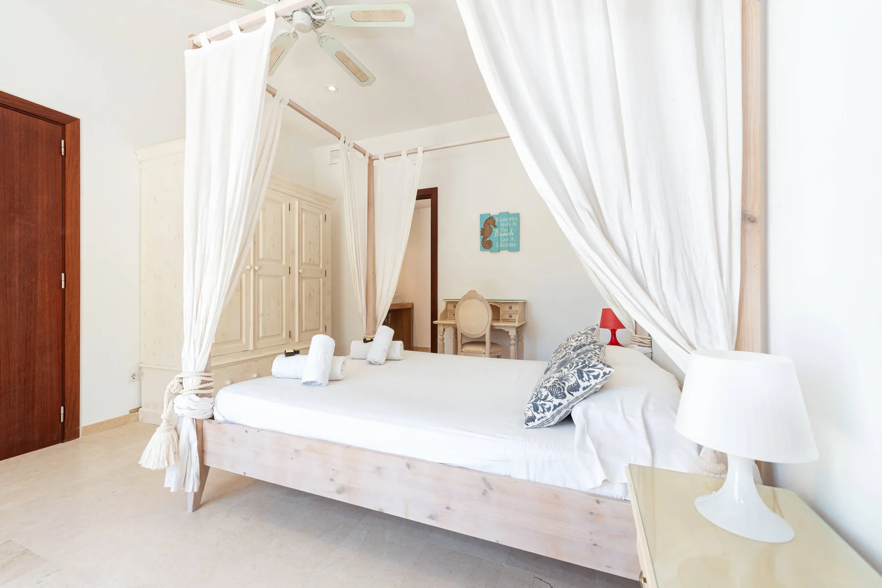 A bright bedroom with a white canopy bed and light curtains.