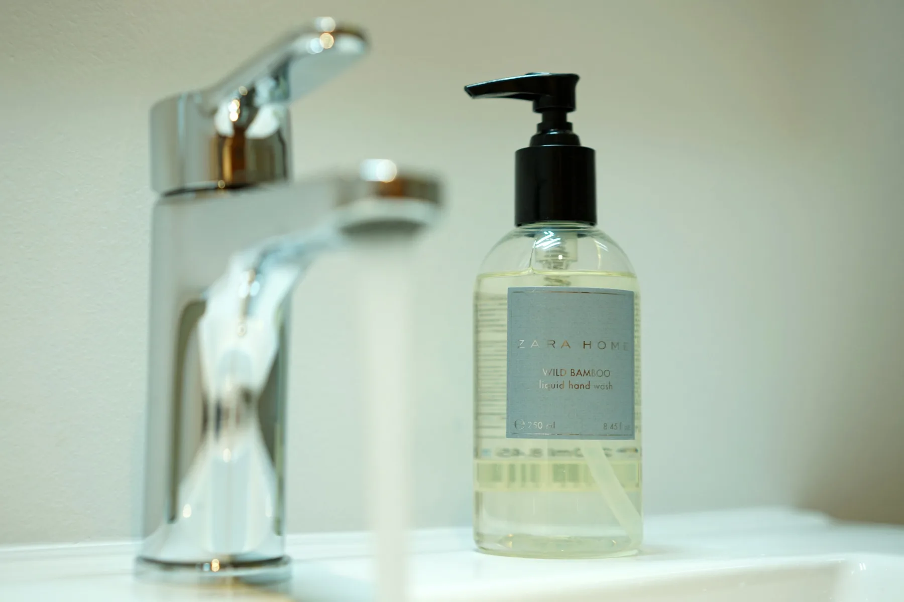 A bathroom sink faucet stands beside a pump bottle of liquid soap.