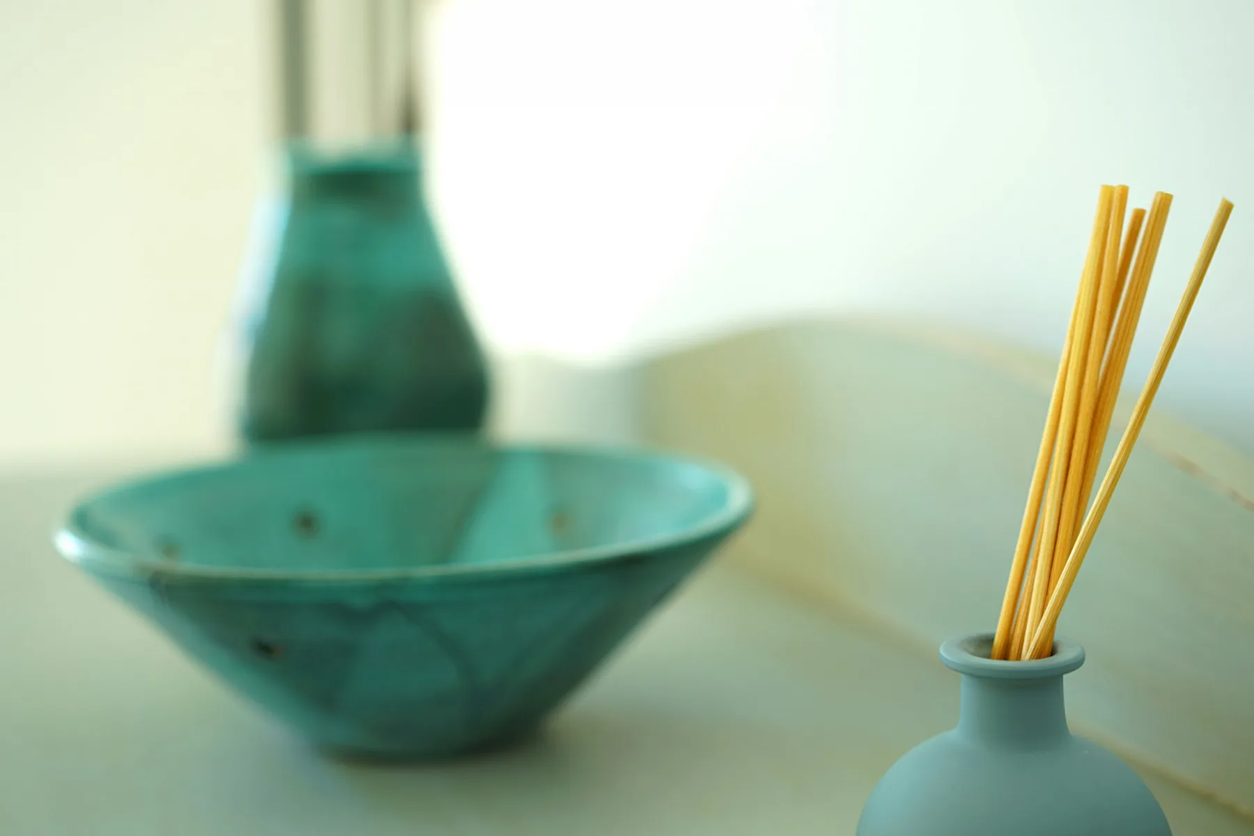 A teal bowl and reed diffuser sit on a pale tabletop.