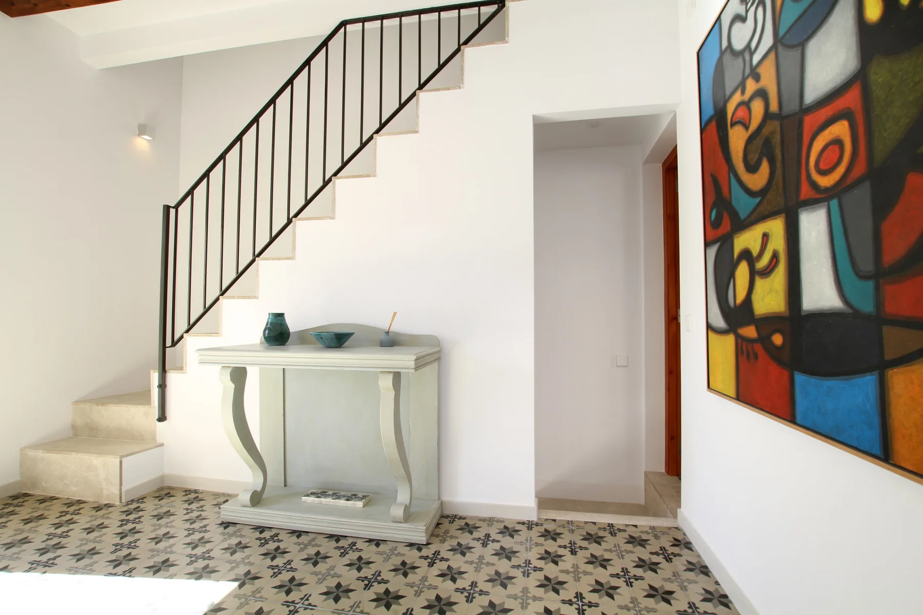 A bright interior hallway with a staircase, console table, and colorful wall artwork.