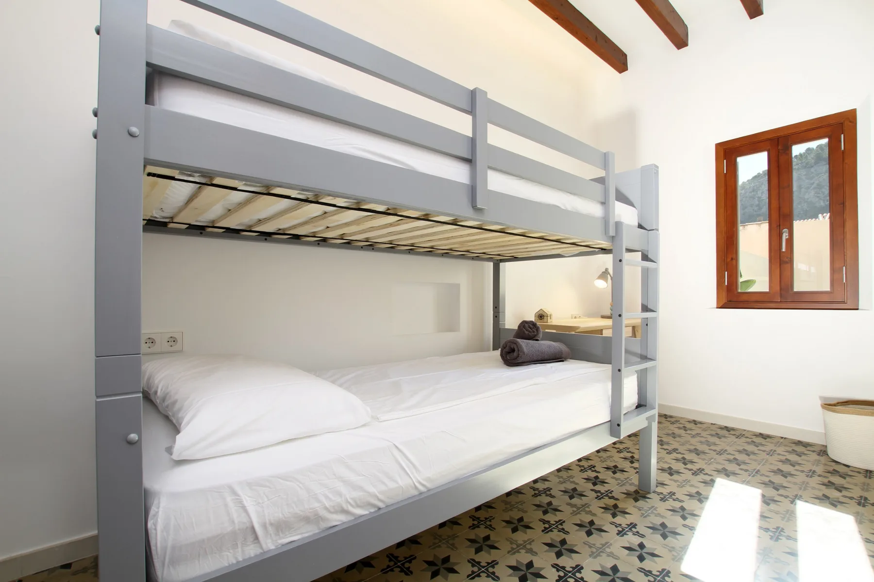 A bedroom with a gray bunk bed, white bedding, and a wooden-framed window.