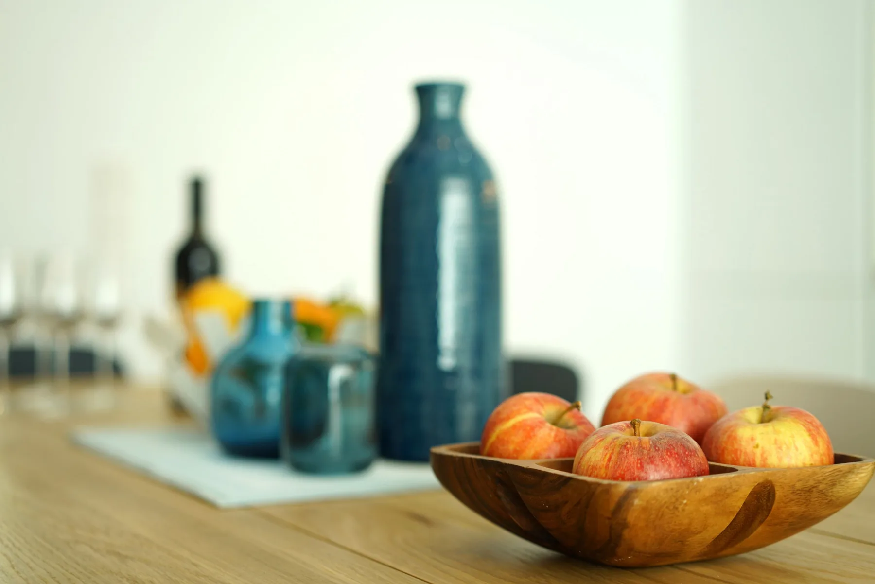 A wooden bowl of fruit sits on a kitchen counter beside decorative bottles.