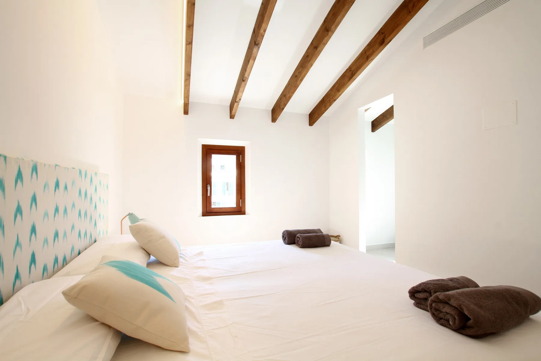 A bright bedroom with a bed, patterned headboard, and exposed ceiling beams.