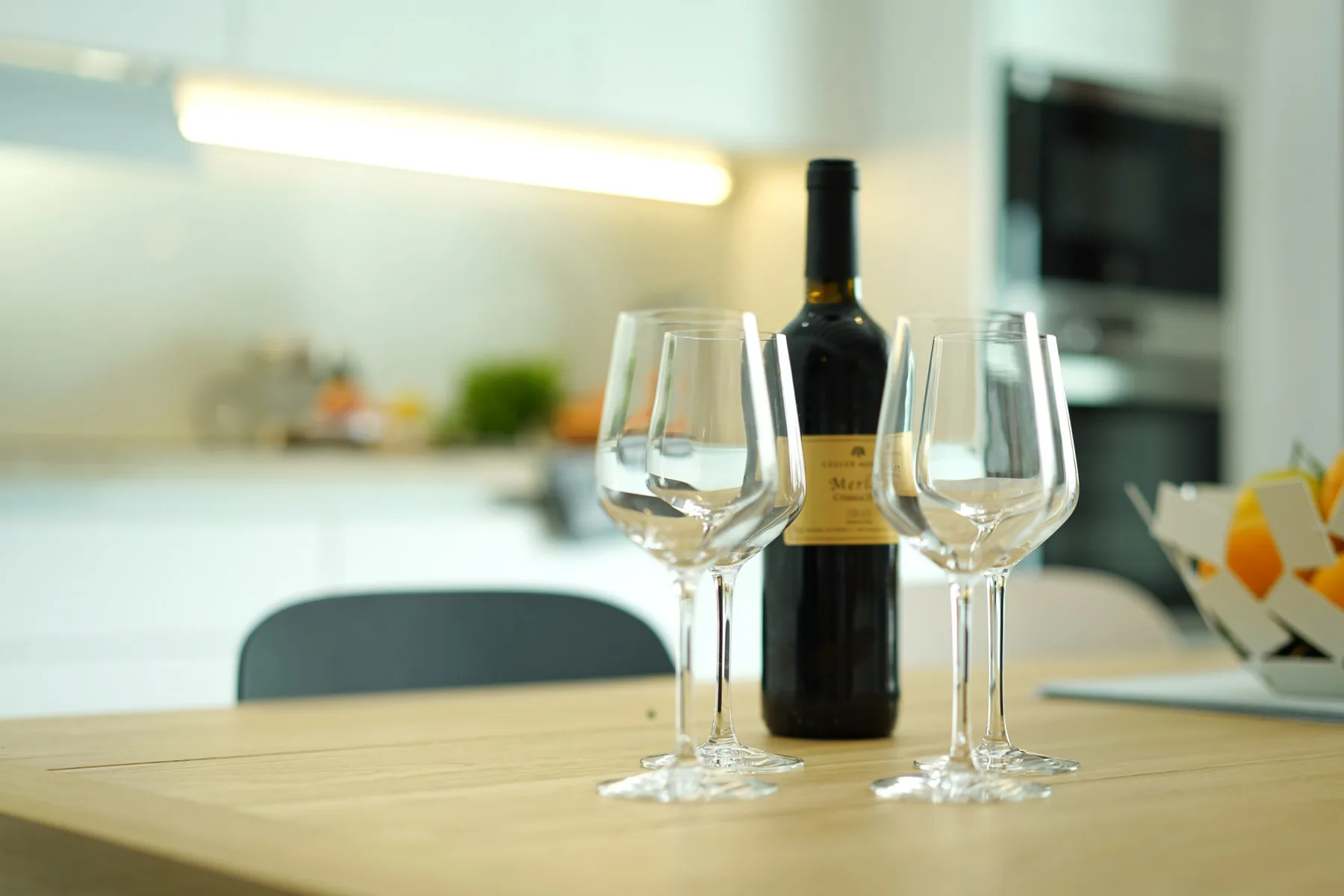 A wine bottle and glasses sit on a table in a bright kitchen.