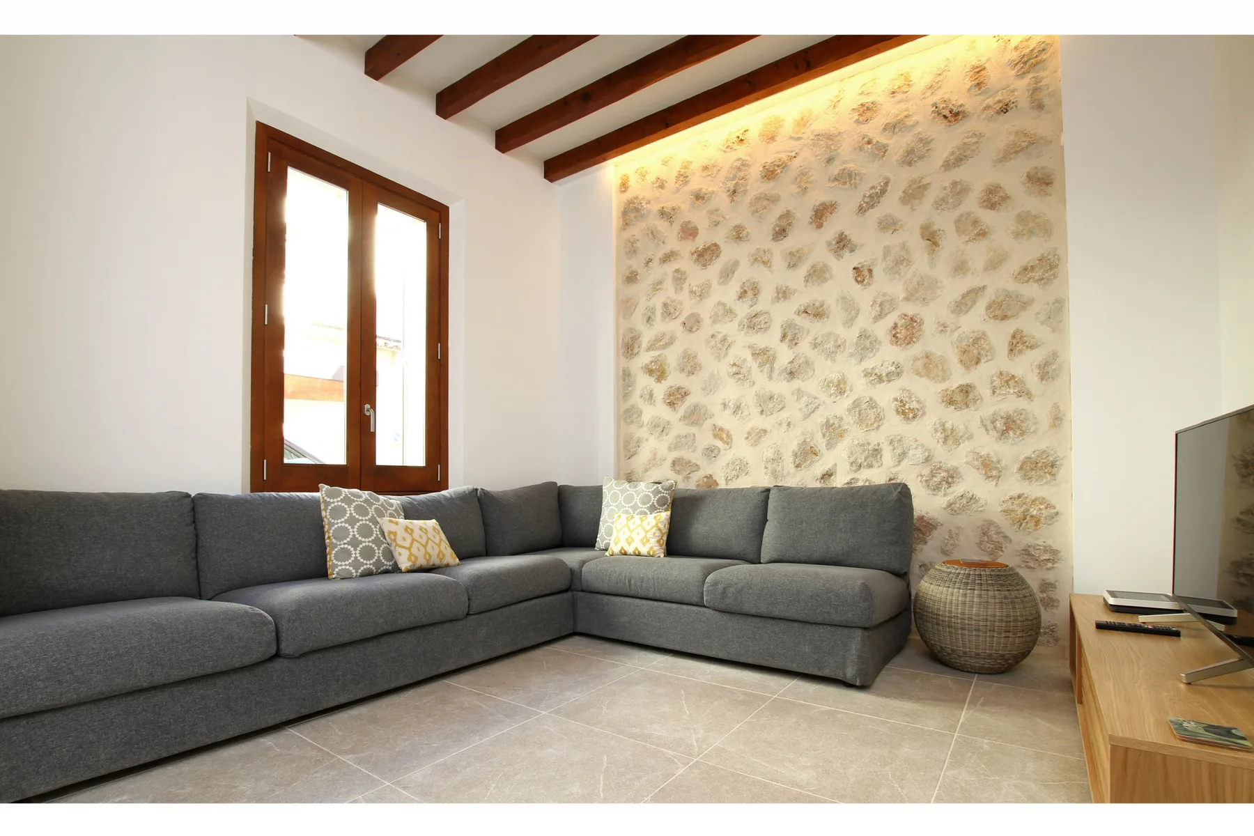 A living room with gray seating, a stone-patterned wall, and exposed ceiling beams.