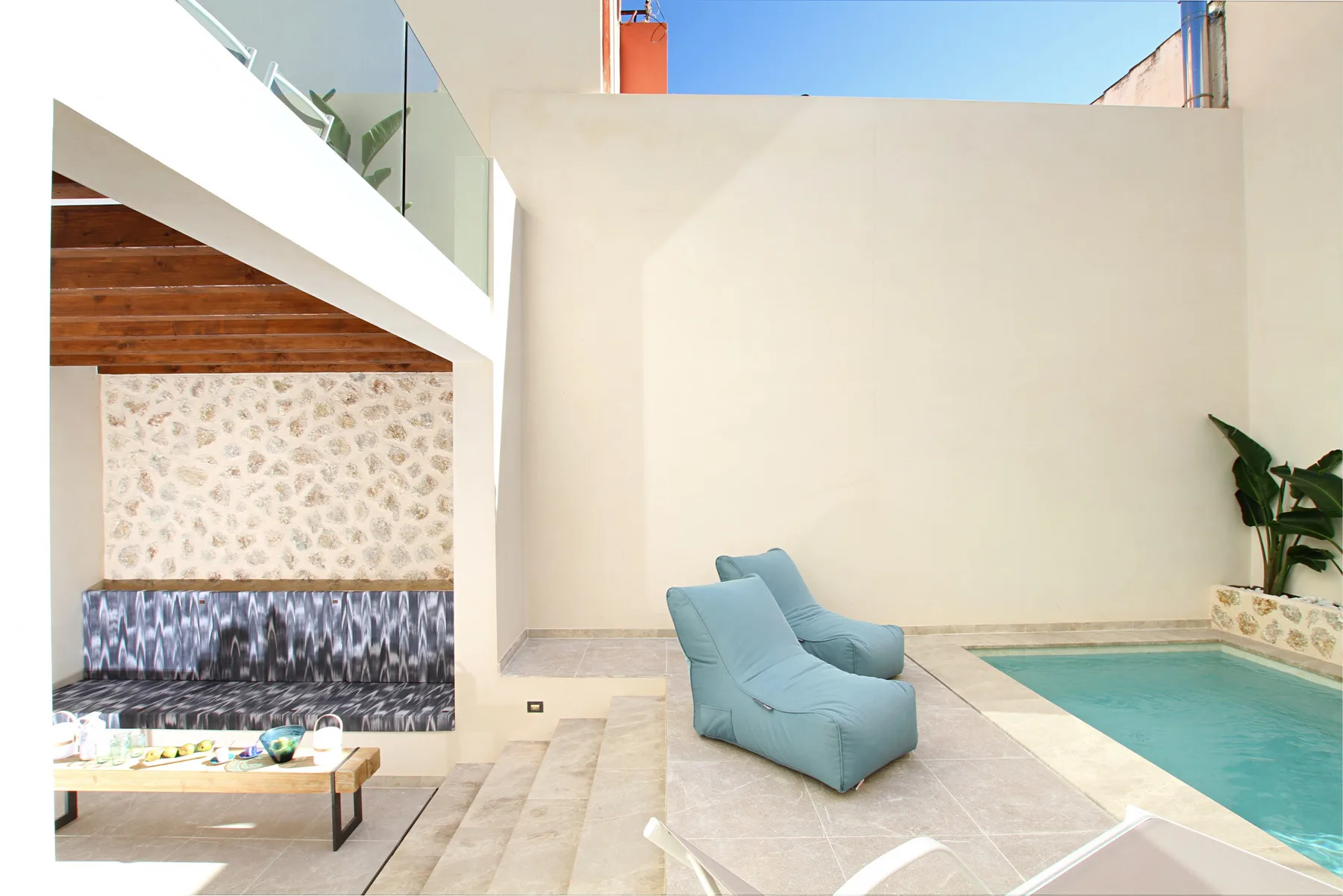 A bright courtyard seating area has a blue lounge chair beside a small pool.