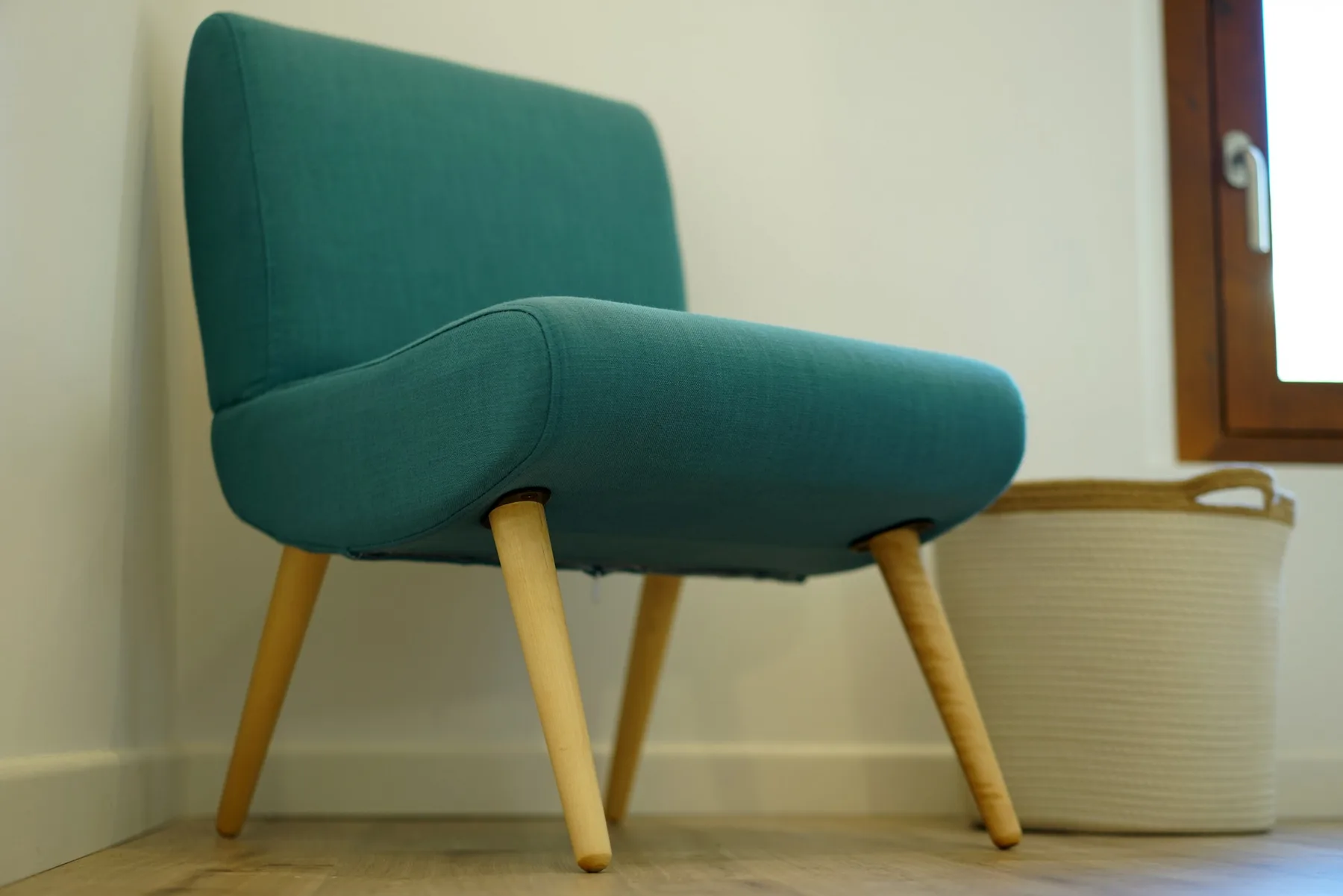 A teal upholstered chair sits beside a window in a simple room.