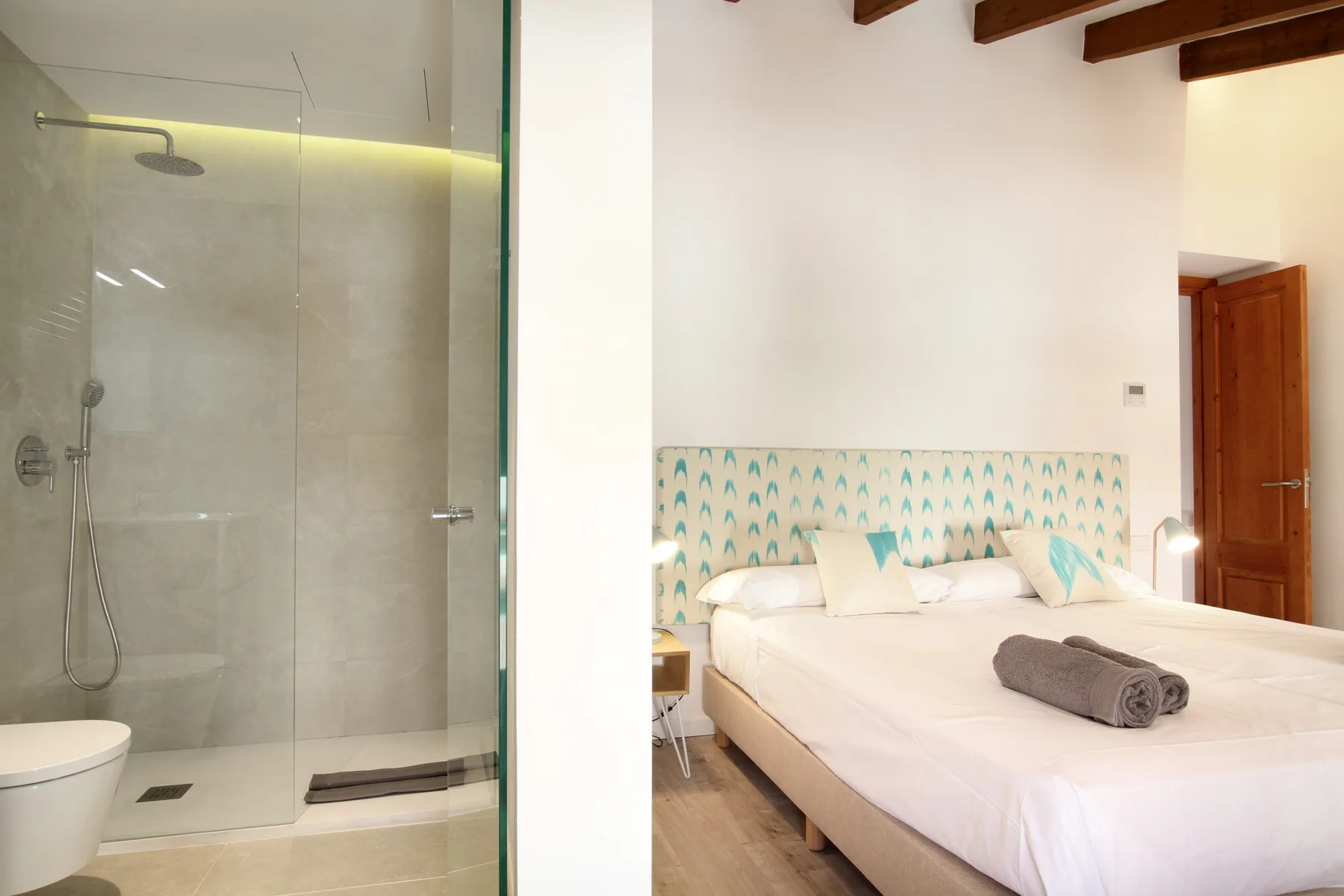 A bedroom with a neatly made bed beside a glass shower.
