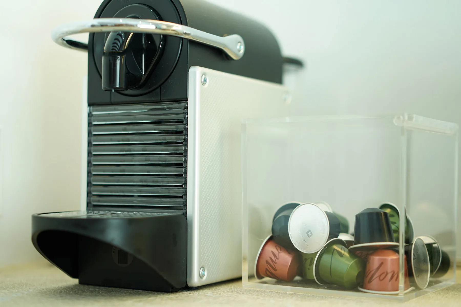 A coffee machine and assorted coffee capsules sit on a light-colored counter.