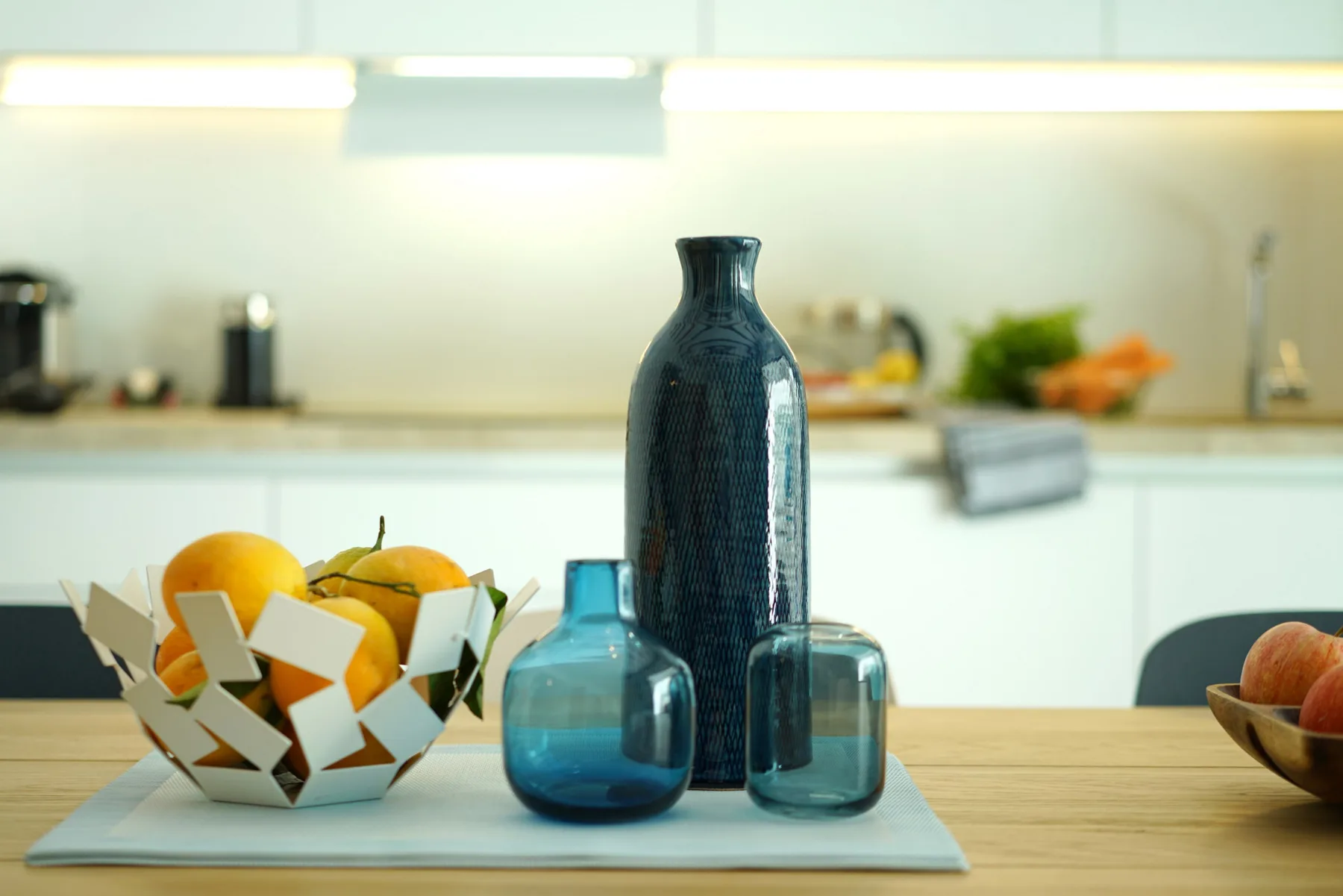 A kitchen counter with decorative glass vases and a bowl of fruit.