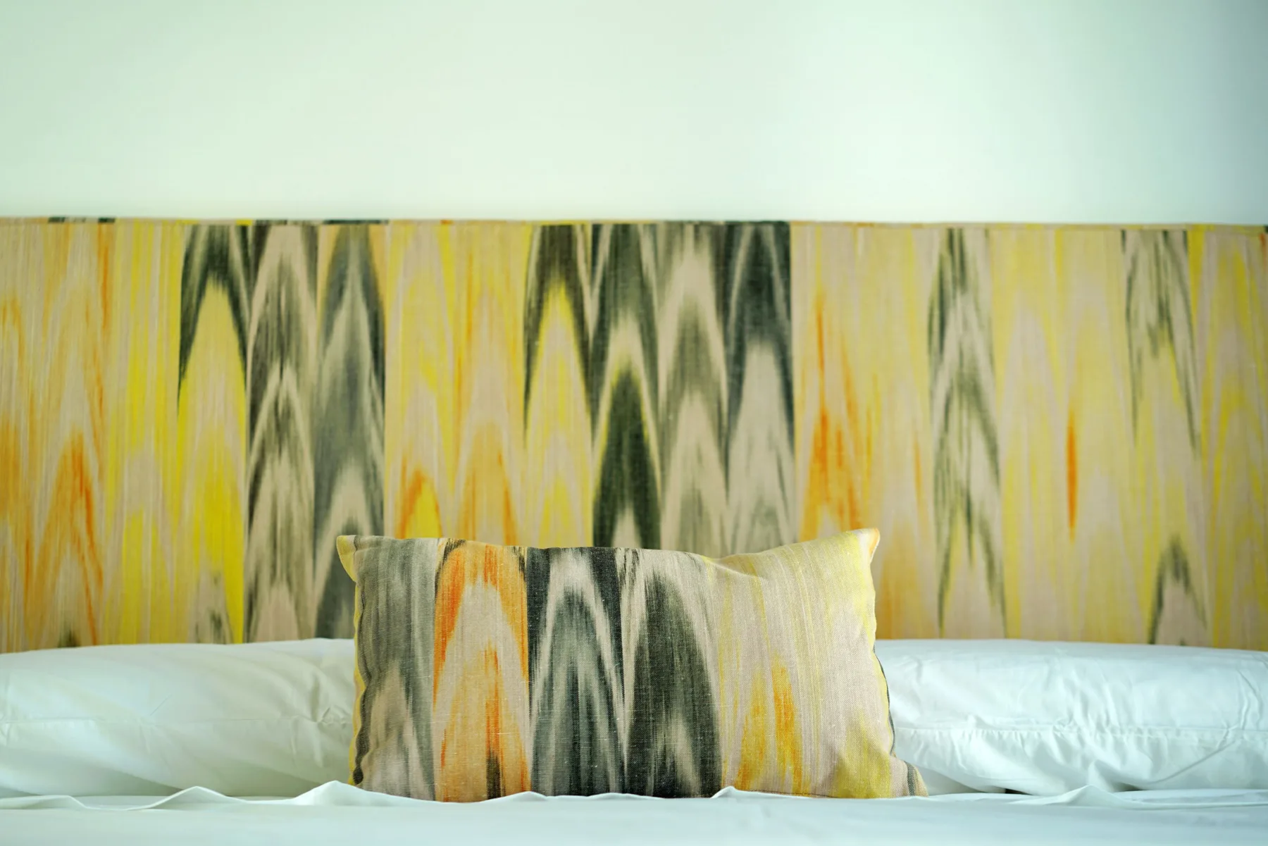 A bed with white bedding and a patterned headboard and decorative pillow.