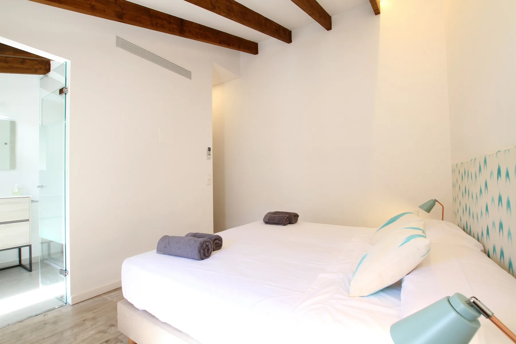 A bright bedroom with a white bed and exposed wooden ceiling beams.