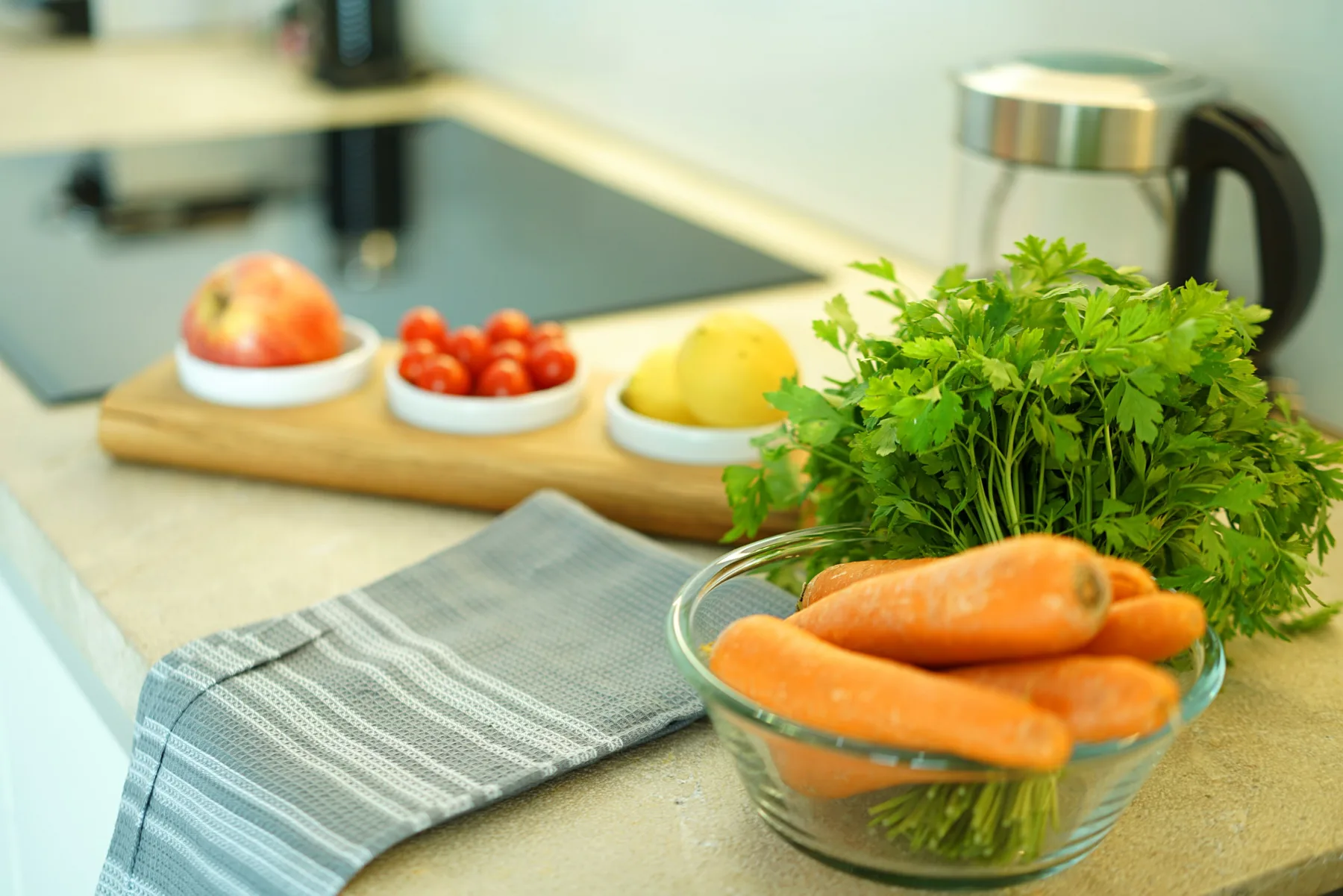 A kitchen counter with fresh carrots, herbs, fruit, and a folded cloth.