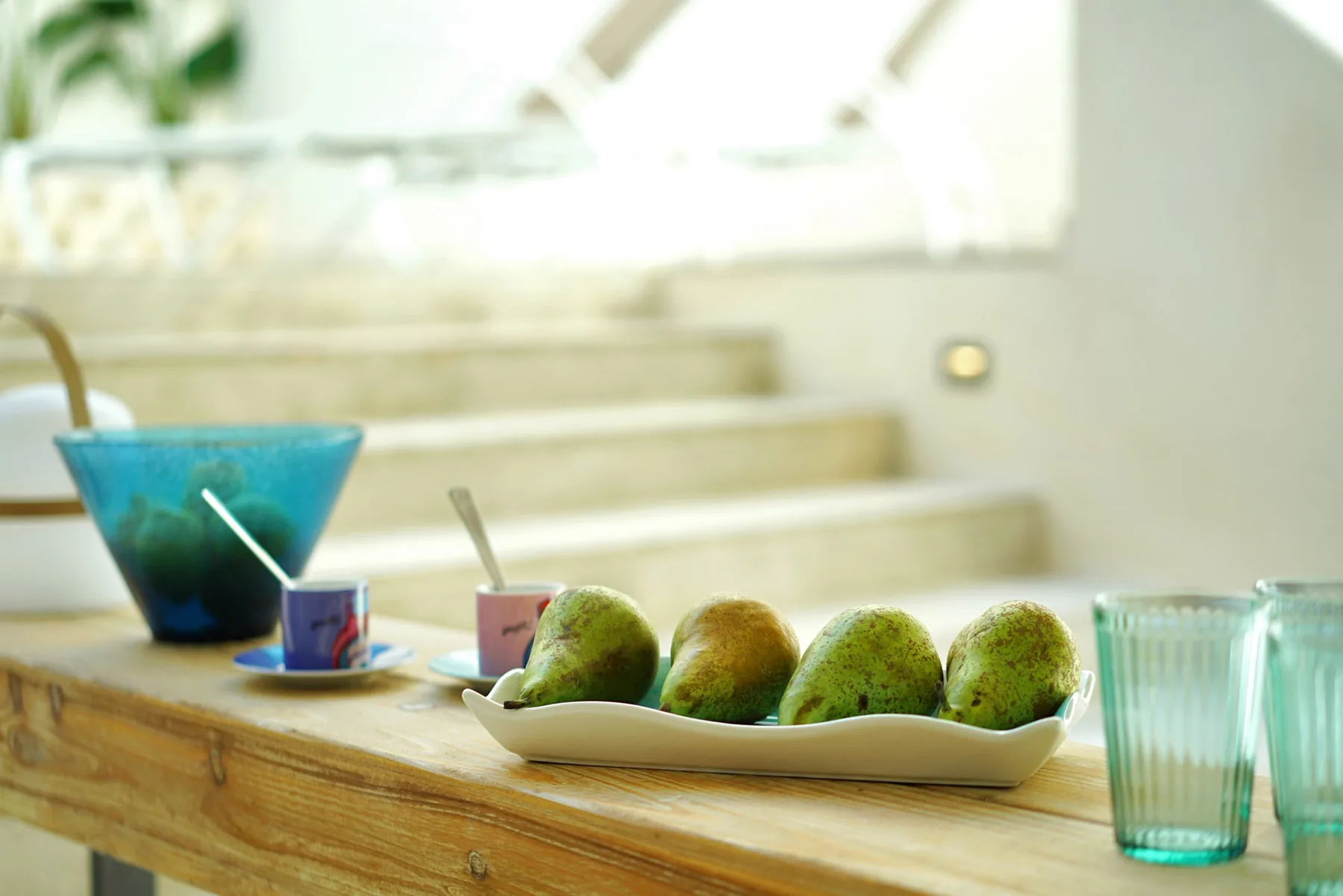 A wooden counter displays a bowl of fruit, colorful dishes, and drinking glasses.