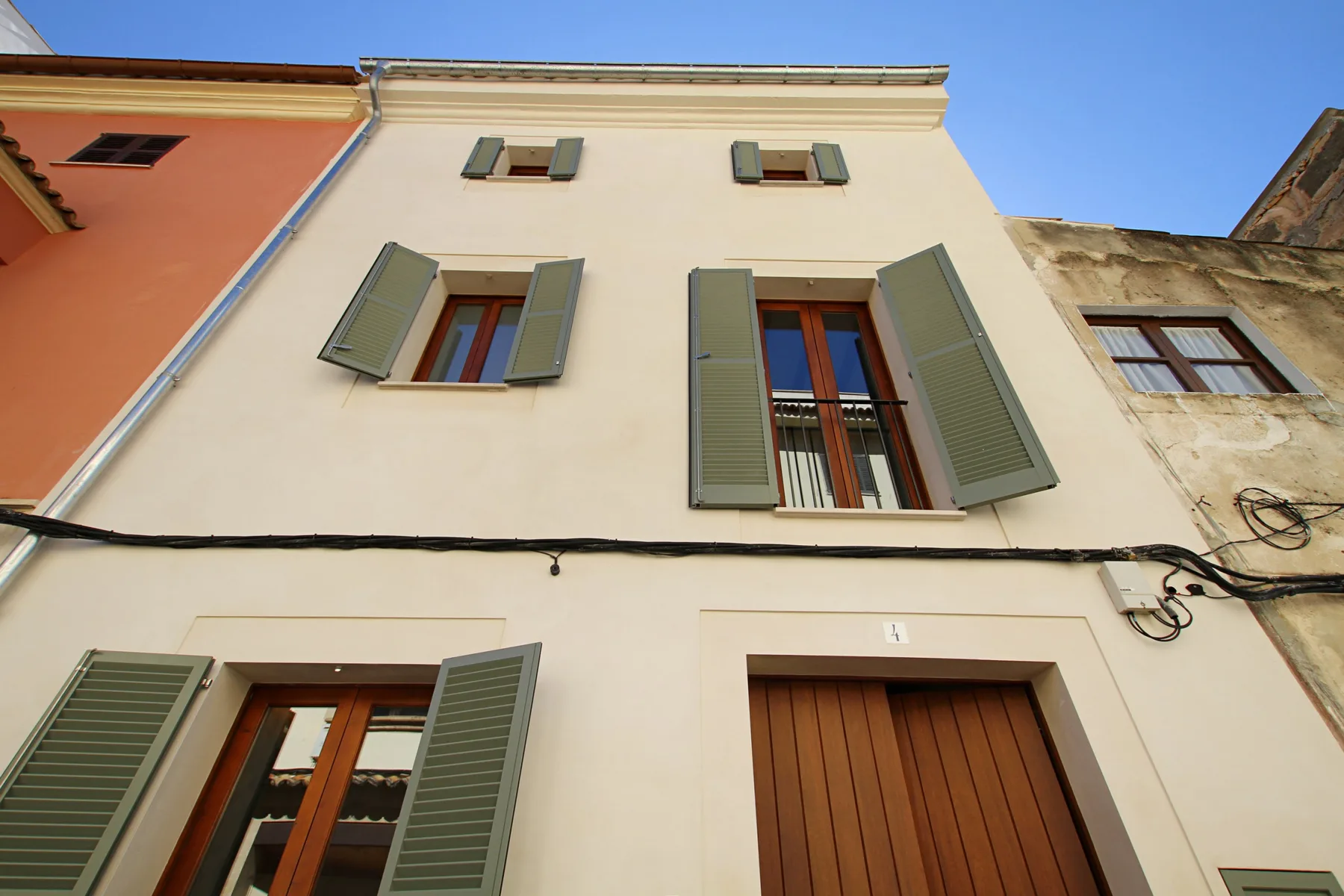 A pale building facade with shuttered windows and a wooden entrance door.