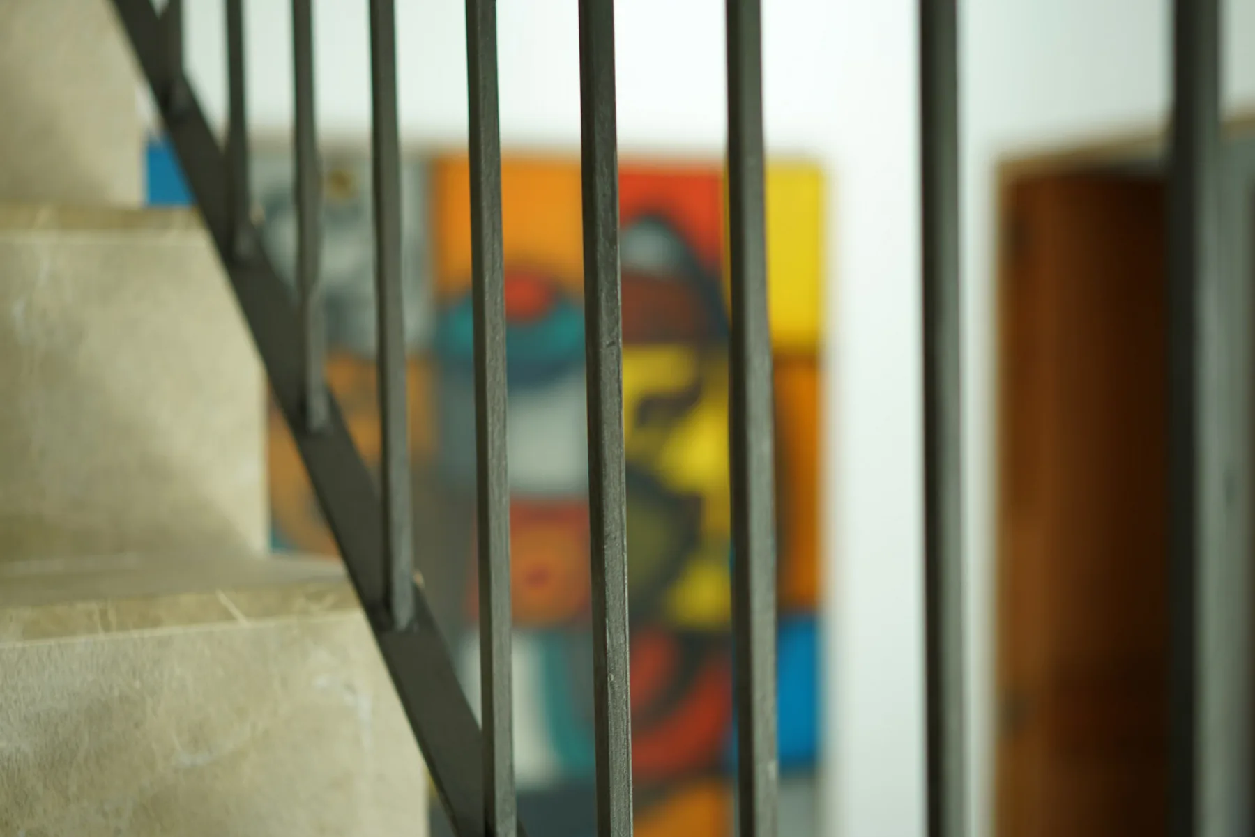 A staircase with a dark metal railing stands beside a colorful abstract painting.
