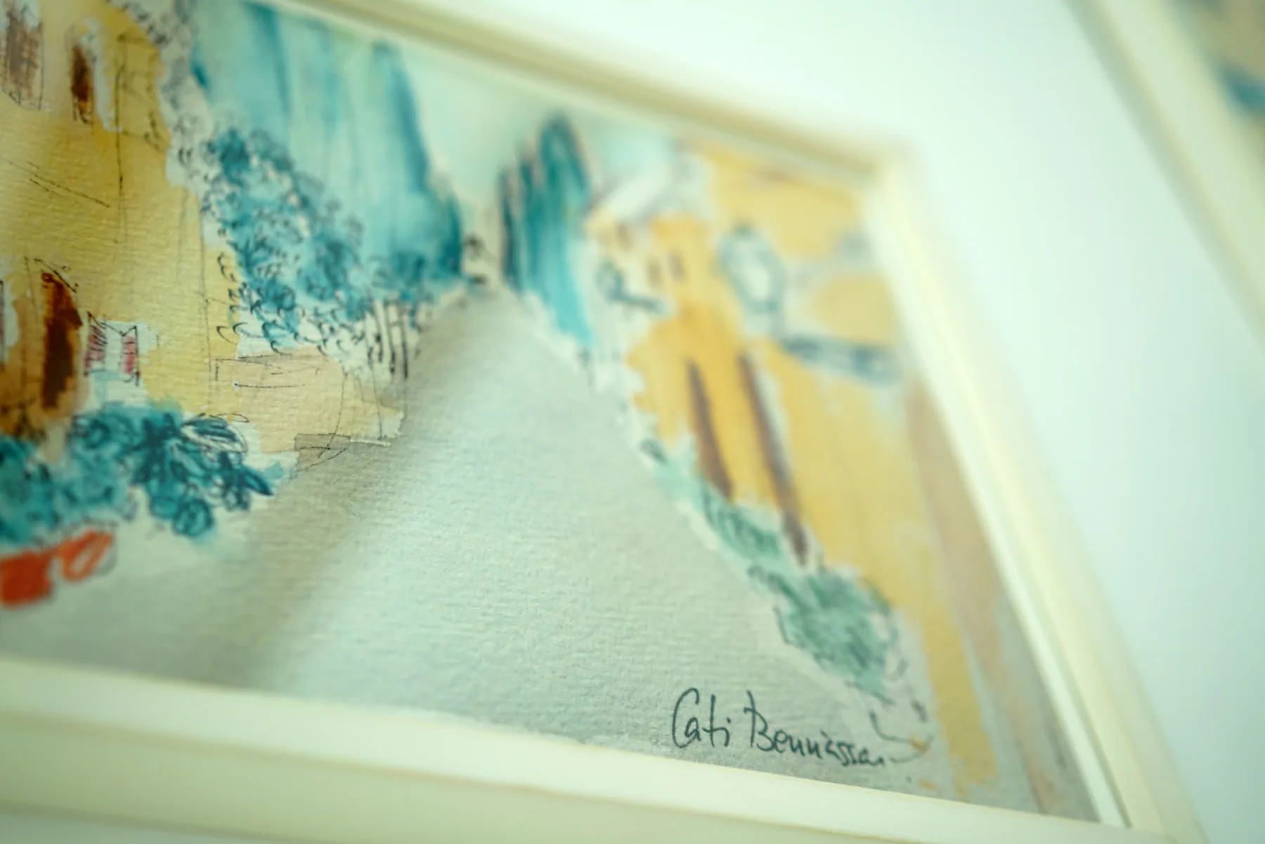 A framed watercolor painting shows a street scene in soft blue and yellow tones.