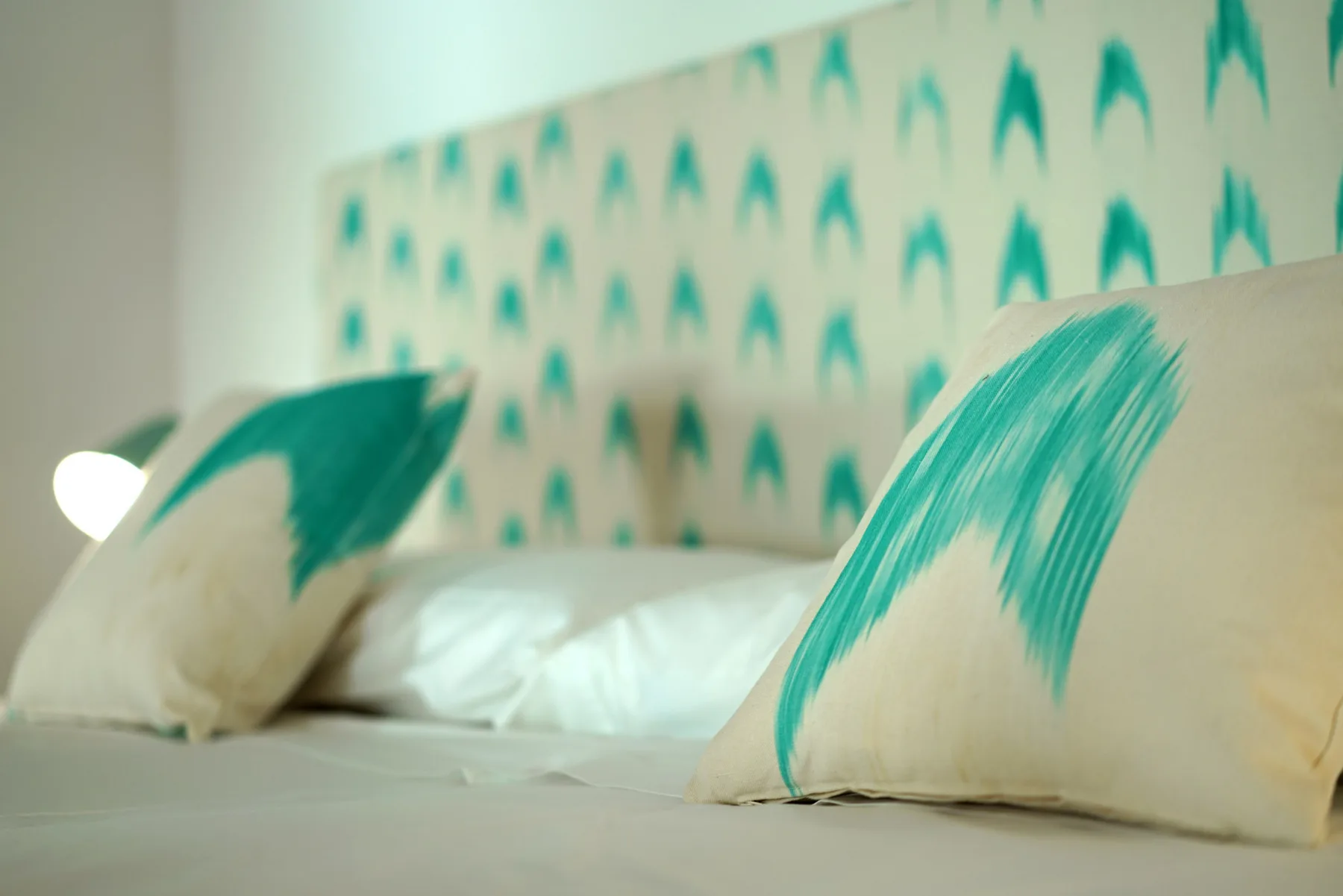 A bed with white bedding and decorative pillows sits against a patterned wall.