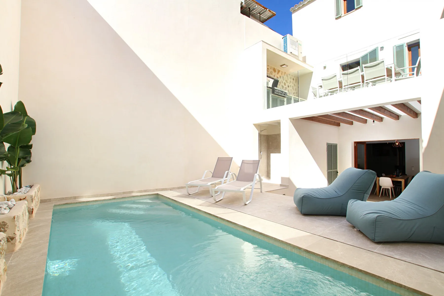 A courtyard swimming pool sits beside lounge seating and a bright white building.